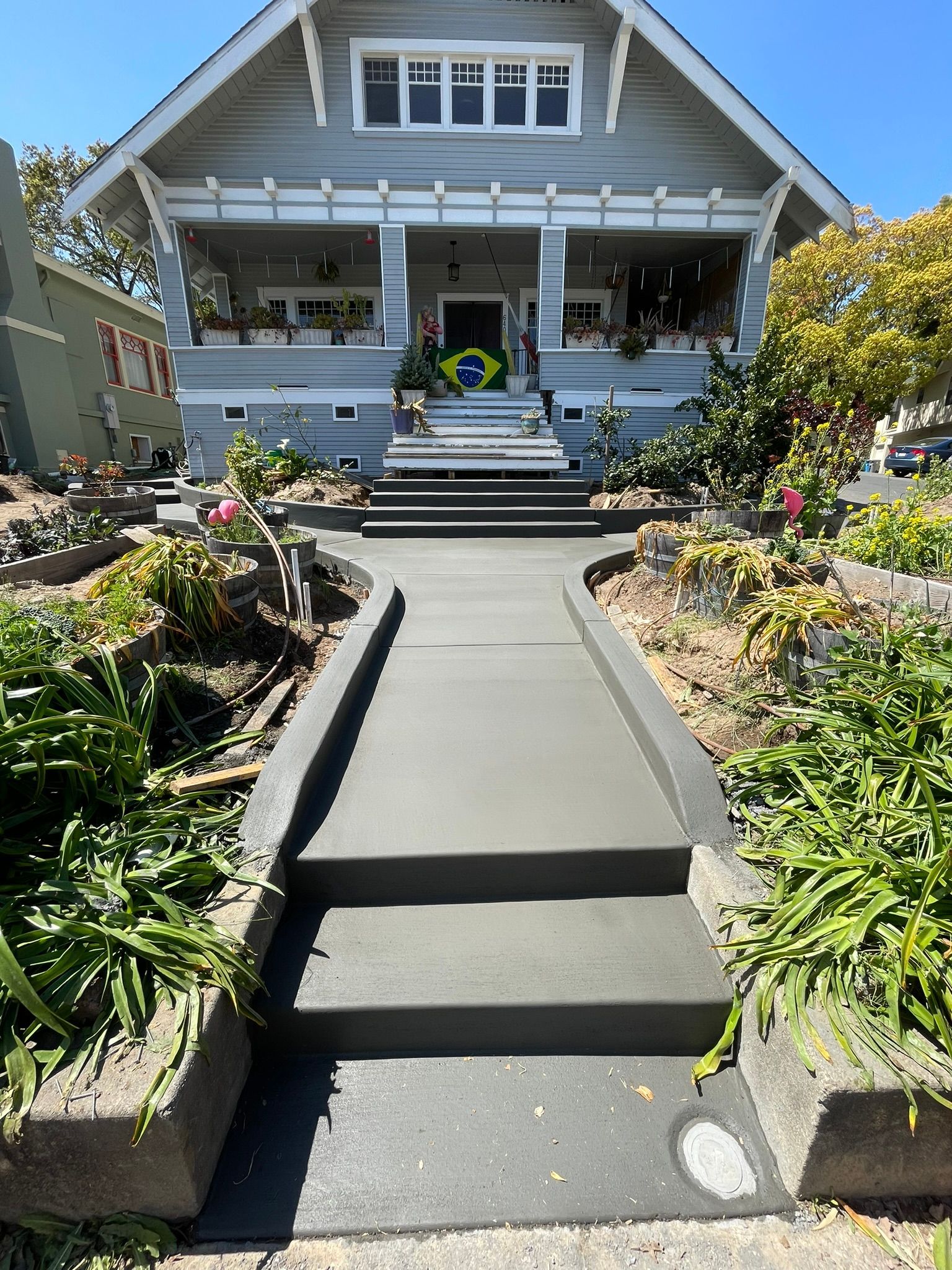 Front walkway leading to a blue house with steps, porch, and colorful landscaped garden beds.