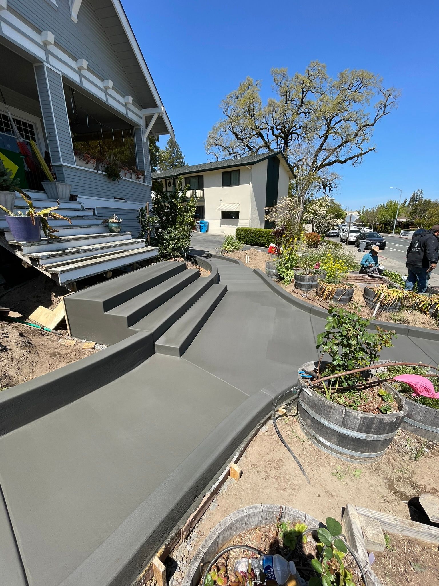 Front yard with concrete steps, potted flowers, and a house under a clear blue sky