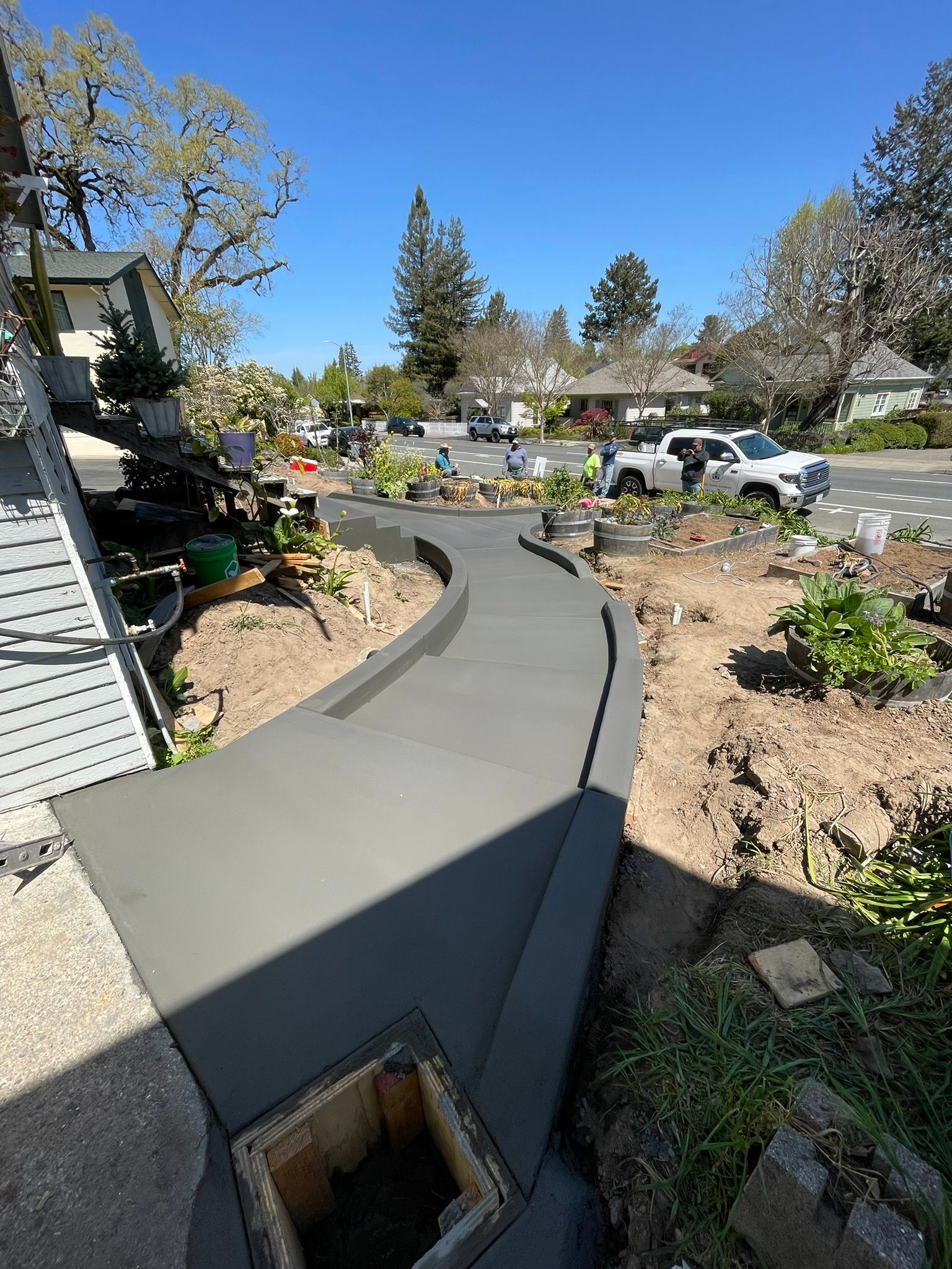 Curved concrete walkway beside a garden bed and driveway in a sunny suburban yard