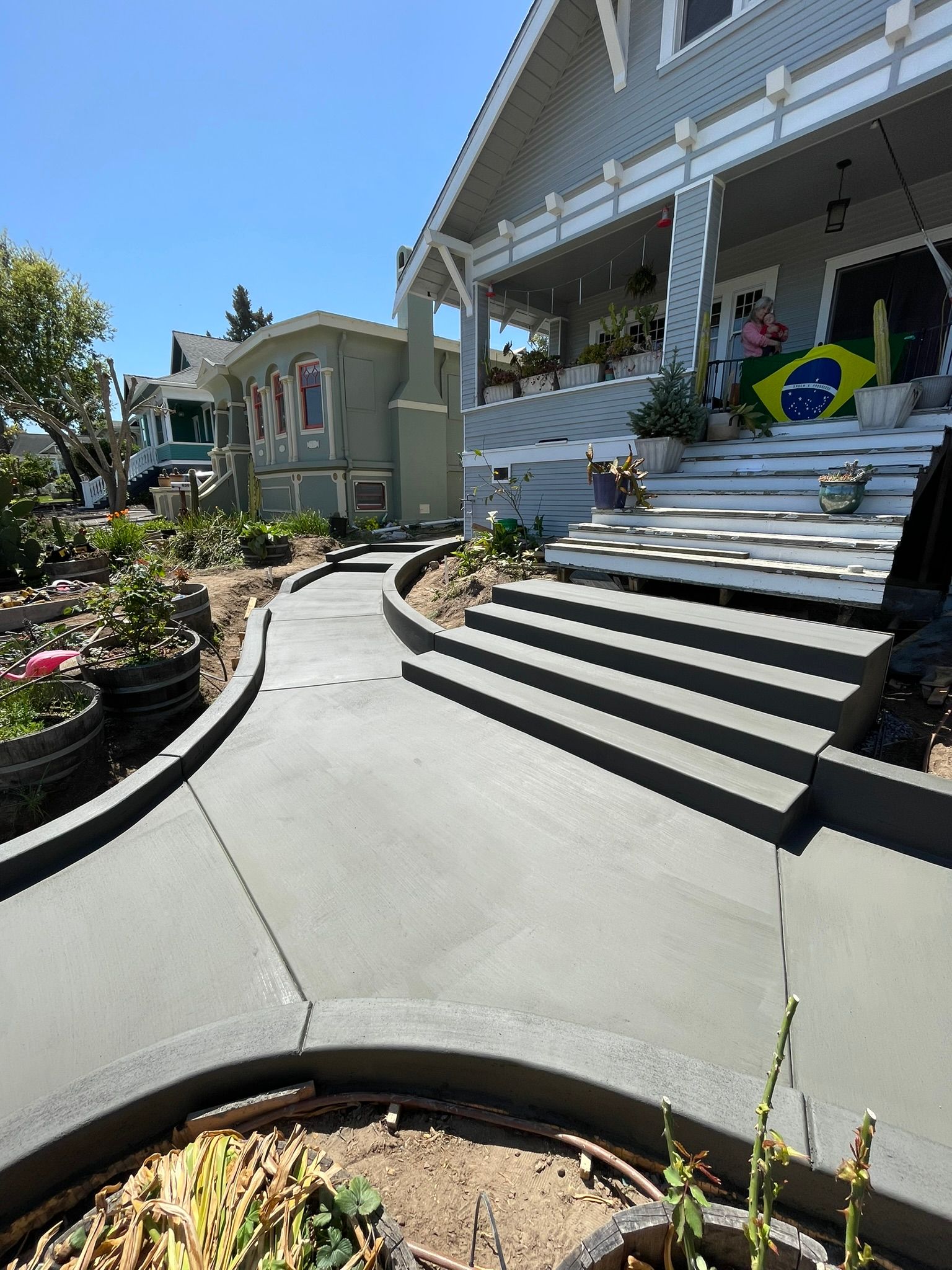 Porch of a large house with stairs, curved walkway, and Brazilian flag under a blue sky