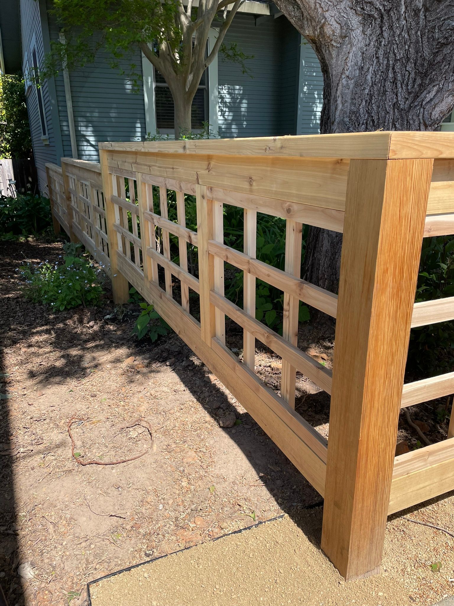 Wooden accessibility ramp with lattice sides beside a house and tree in a shaded yard