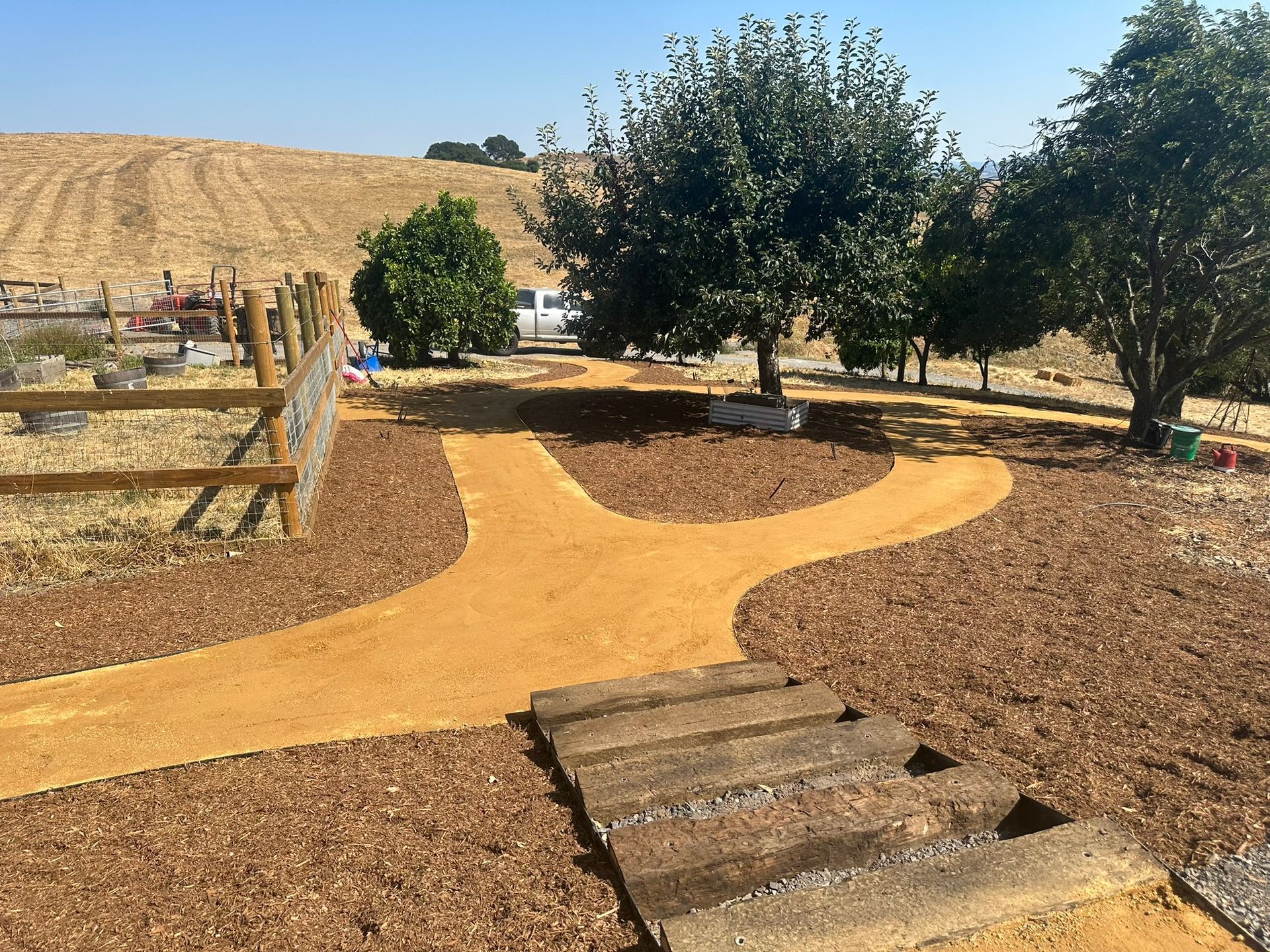 Garden path with a Y-shaped tan walkway, wooden steps, and trees in a dry landscape.