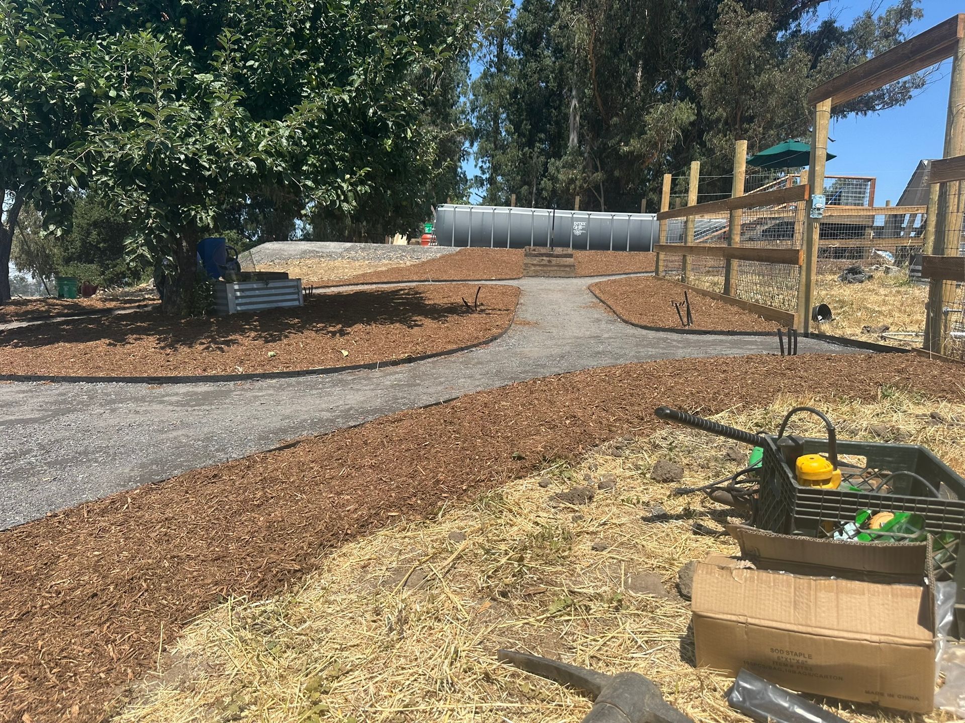 Curving gravel path through a landscaped park with trees, mulch, and wooden play structures under construction