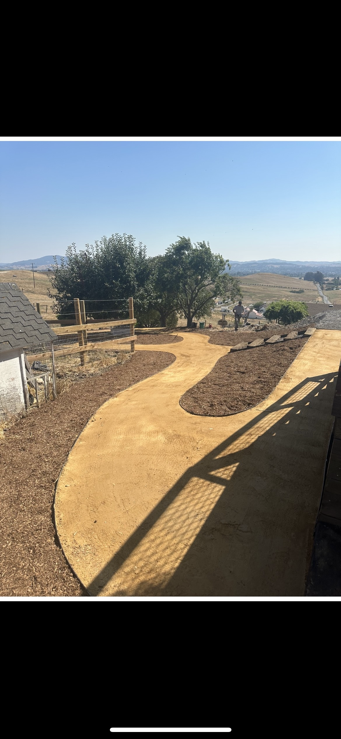 Curved gravel path in a dry hillside yard with trees and distant city views.