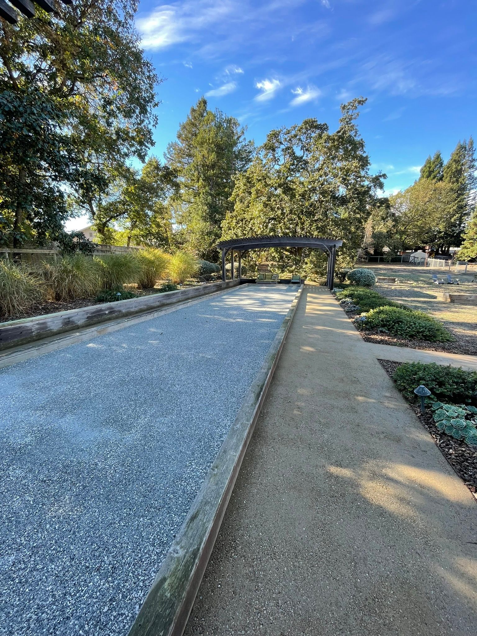Gravel garden path beside a trimmed hedge and trees under a blue sky