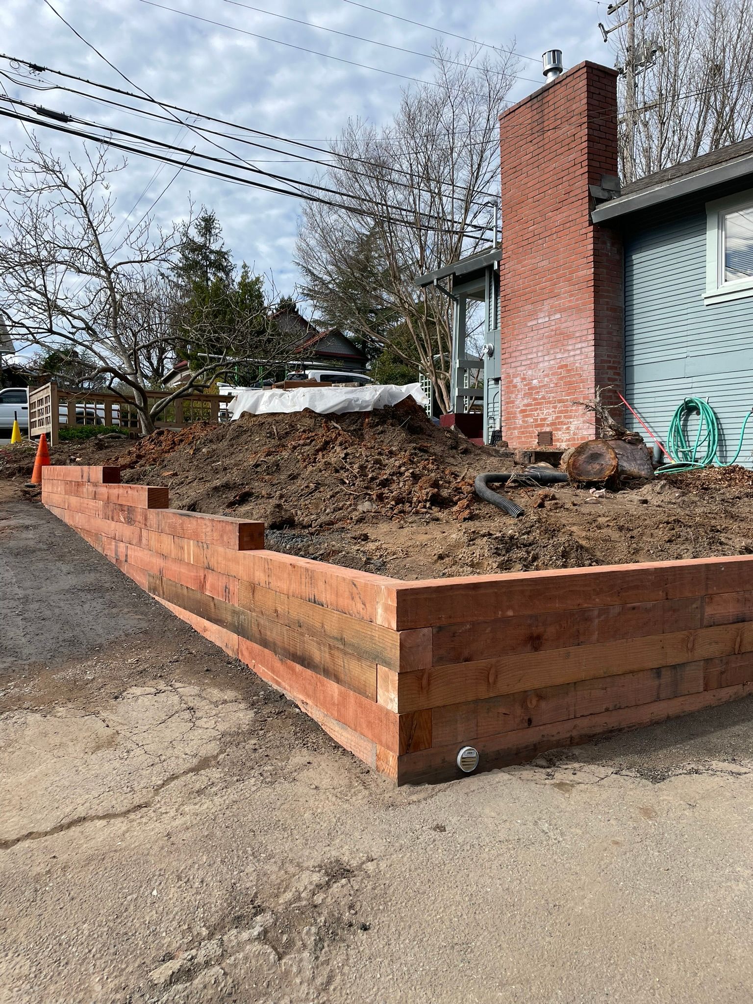 Corner of a house with a raised brick planter and leaf-covered garden bed beside a driveway