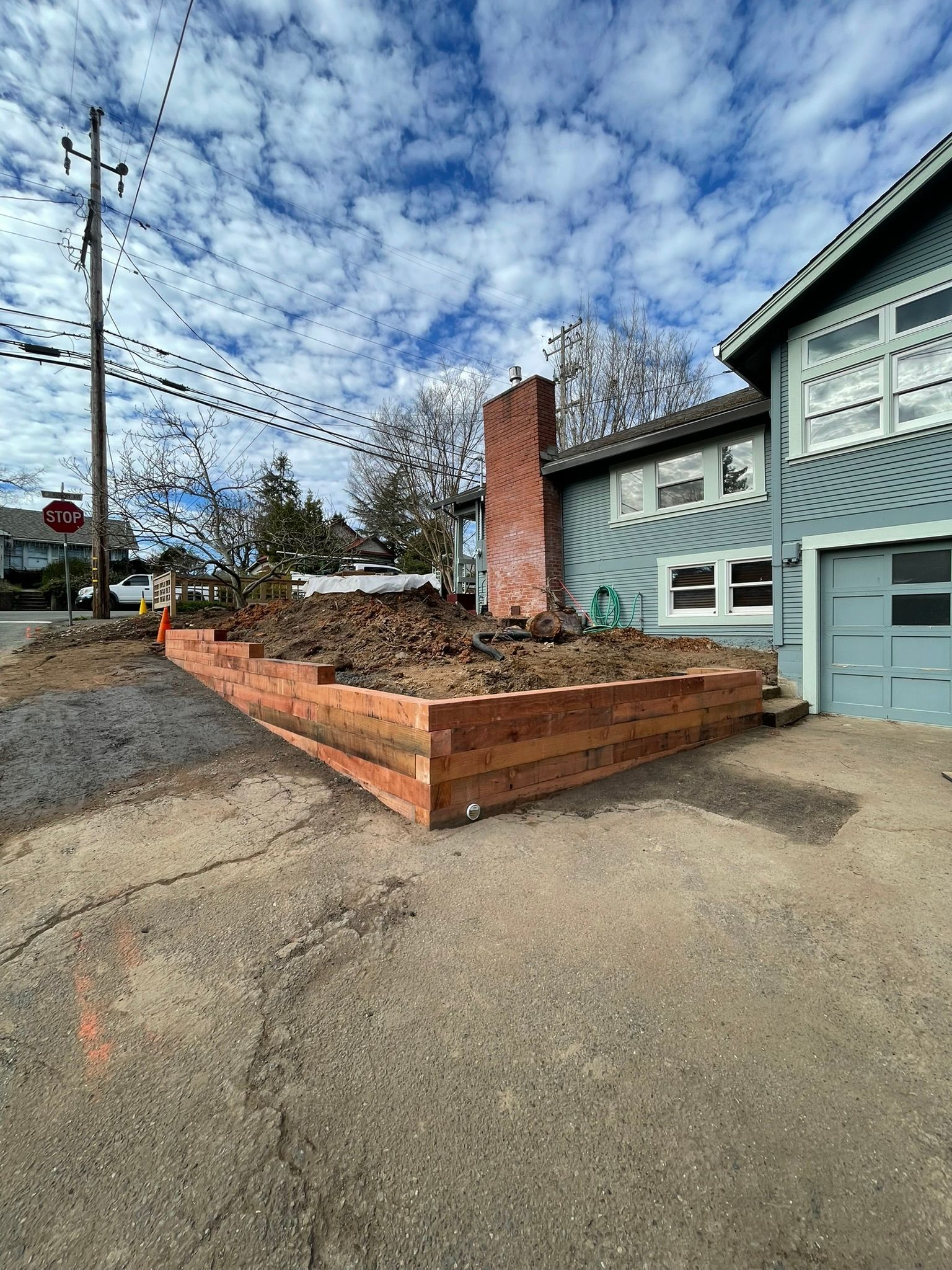 Brick planter wall beside a teal house and driveway under a cloudy sky