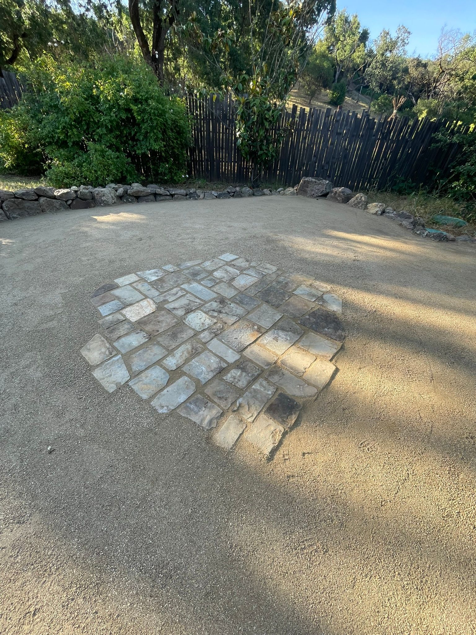 Sunlit gravel path with a small patch of cobblestones near dense green bushes