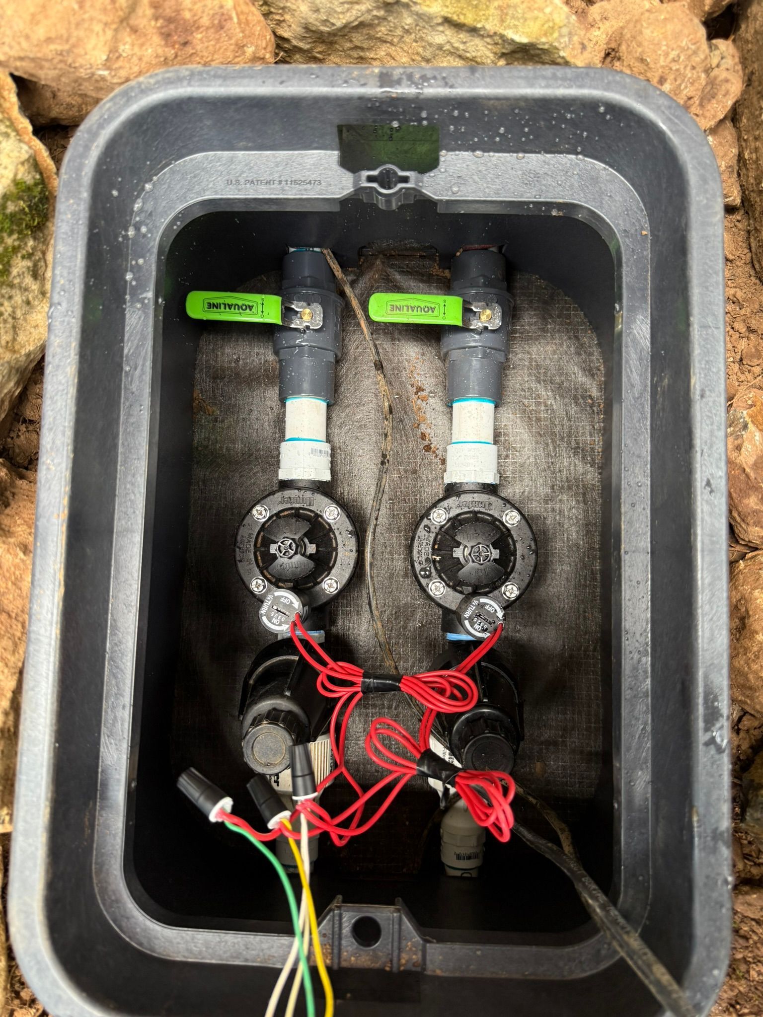 Two green-handled valves and connected red wires inside a black utility box.