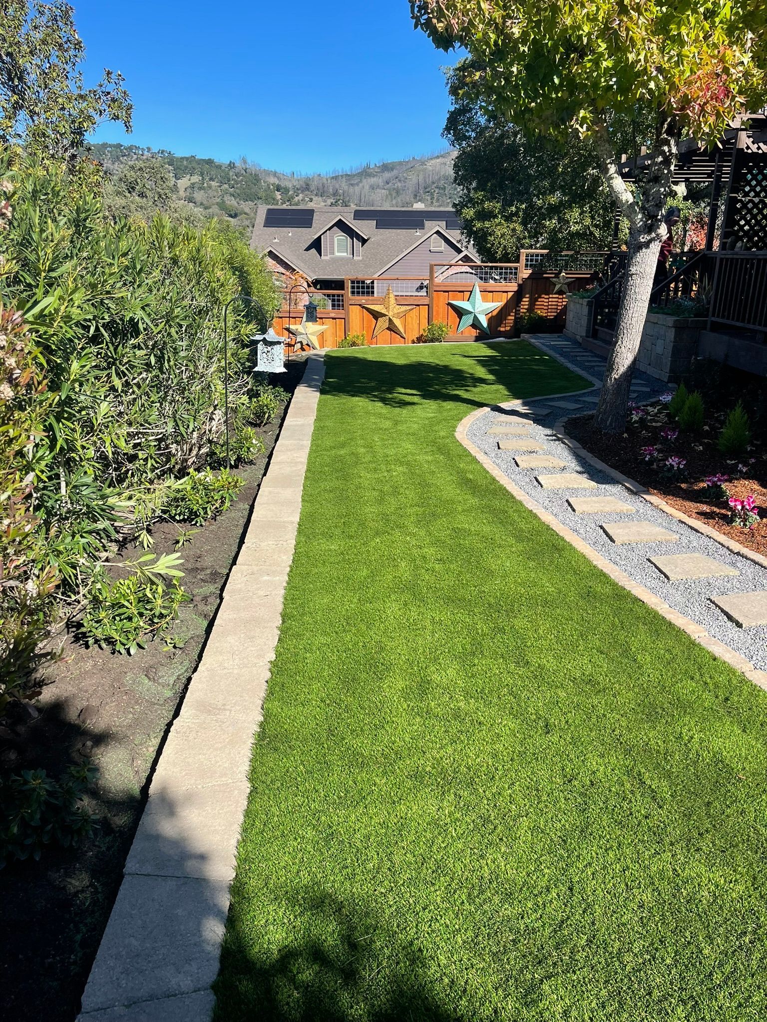Backyard lawn with stone borders, garden beds, and houses in the background under sunny skies