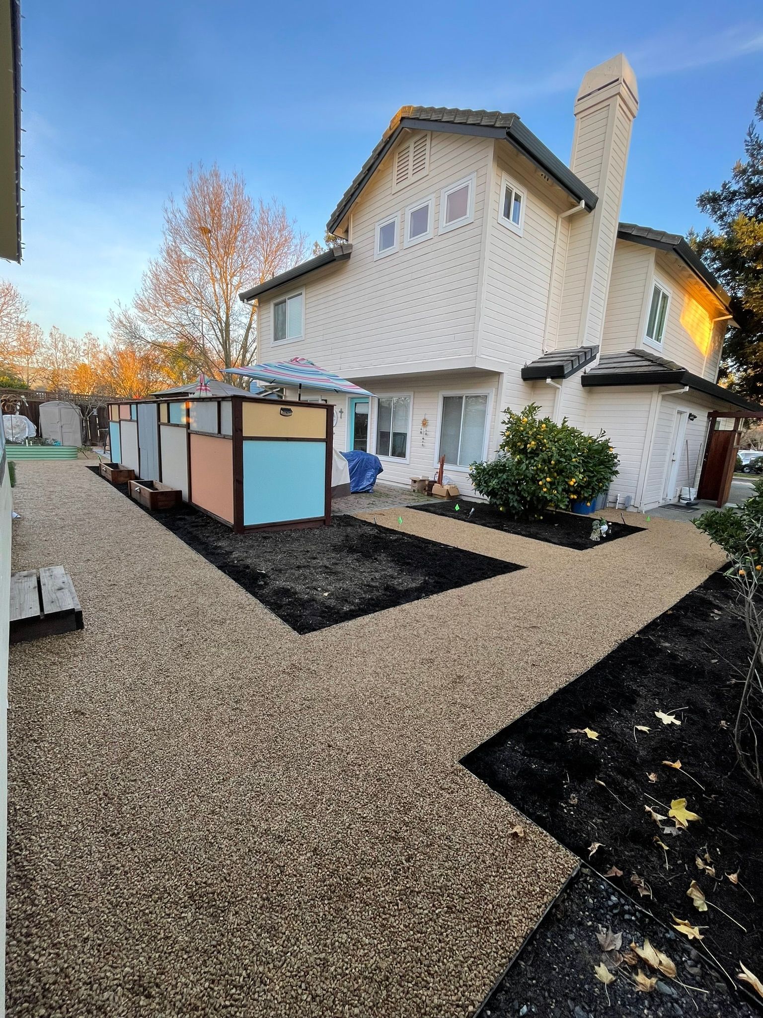 Gravel yard path leading to a two-story house with light siding and autumn trees nearby