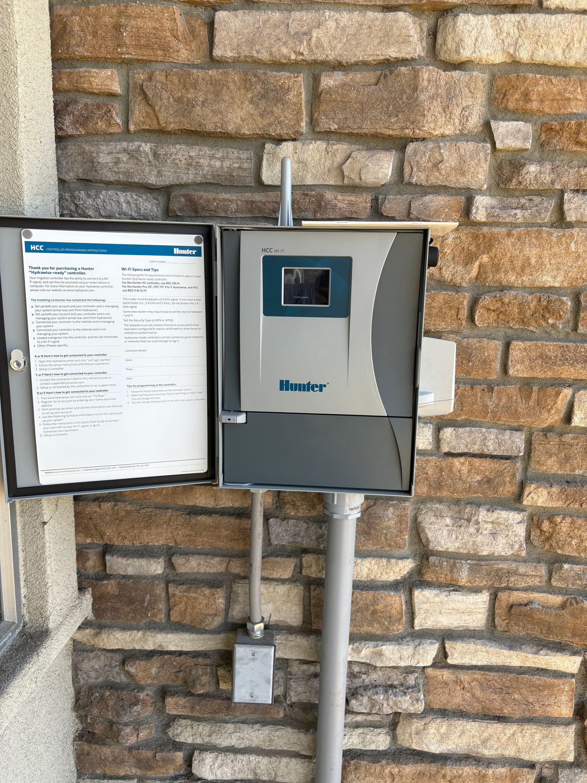 Intercom keypad and speaker mounted on a stone wall beside a posted instruction sign