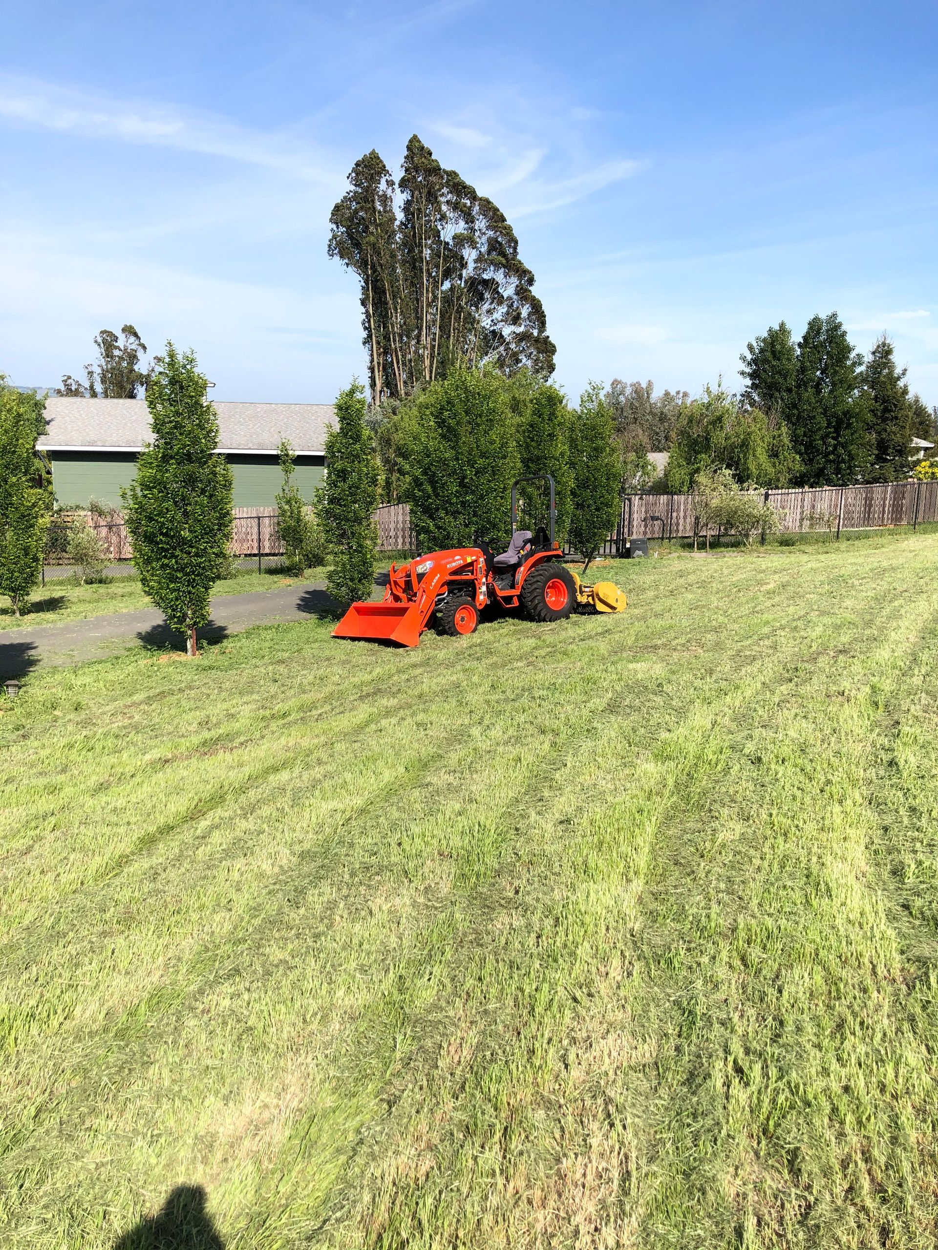 Orange tractor mowing a green field with trees and a fence in the background