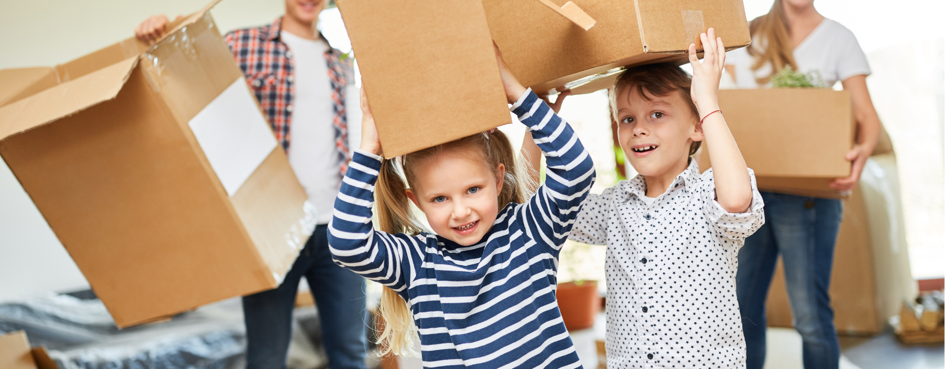Family moving boxes in a new home, children balancing boxes on their heads, smiling.