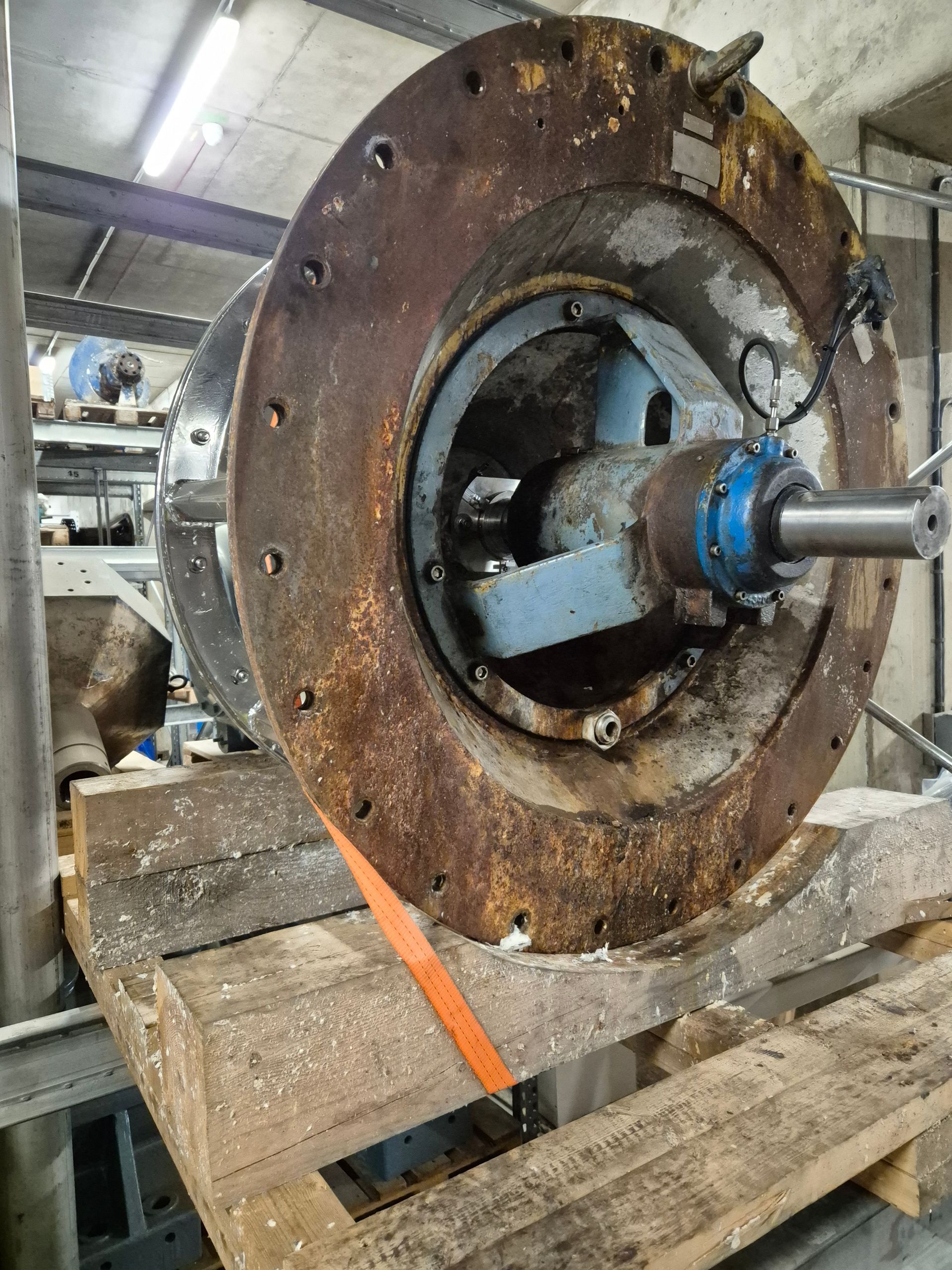 Rostig industriell pump eller motor på en träpall i en verkstad, med en axel som sträcker sig från mitten