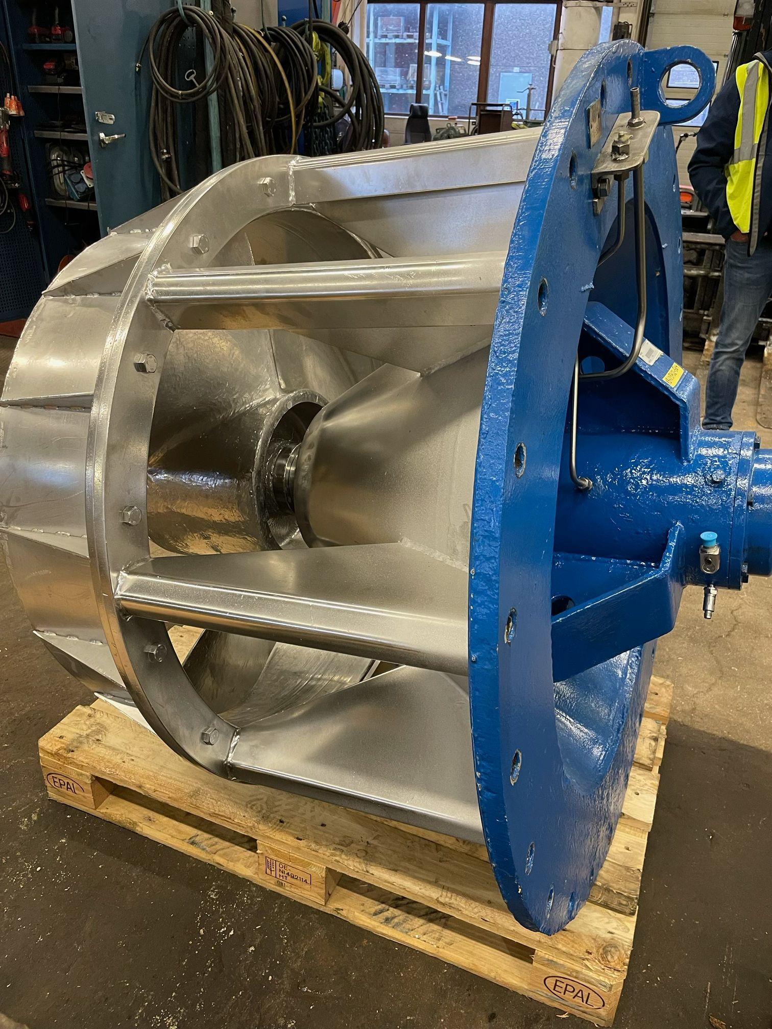 Industriell metallimpellerenhet på en träpall, med en blå monteringsram i en verkstad.