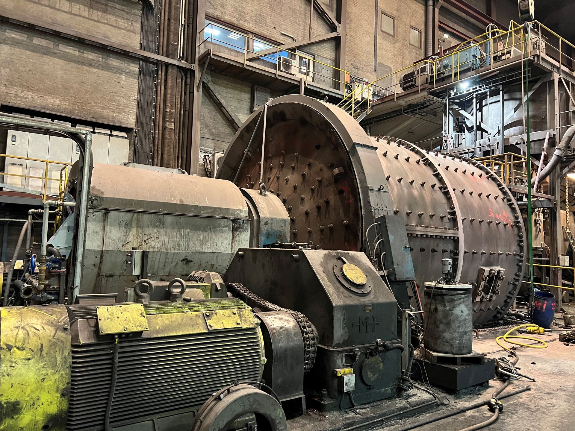 Stor industrimaskin i en fabrik, med en enorm cylindrisk trumma och metallutrustning som omger den.