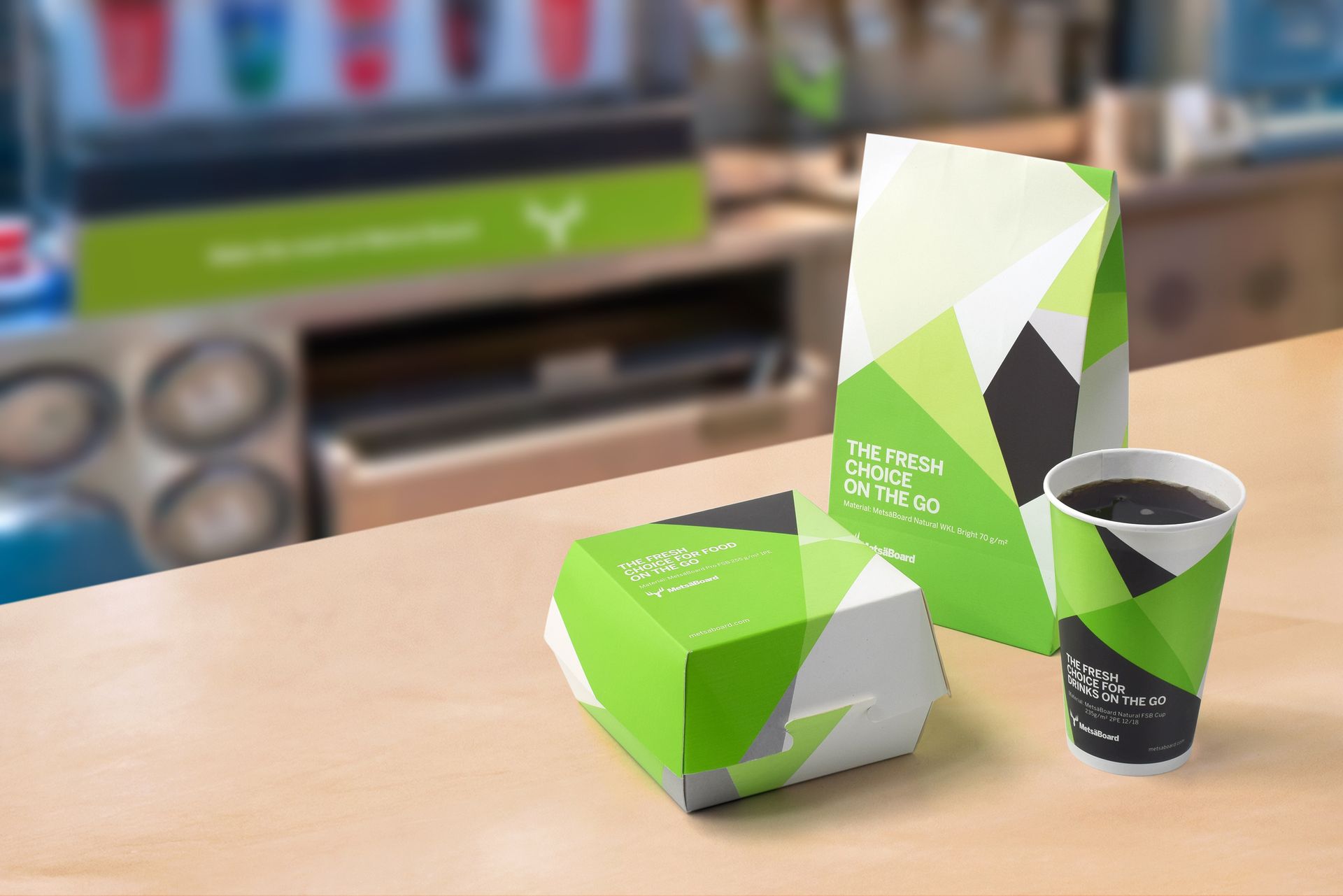 Gröna och vita märkesförpackningar för avhämtning och en kopp på en disk i en kafékiosk