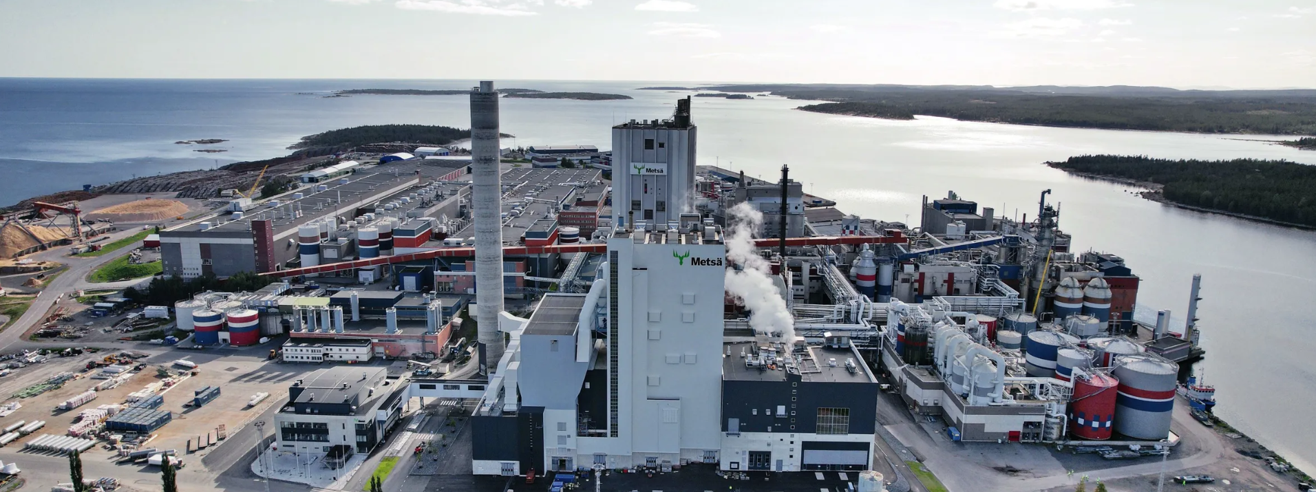 Flygfoto över en industriell hamn vid floden med skorstenar, lager och en bred flod vid solnedgången