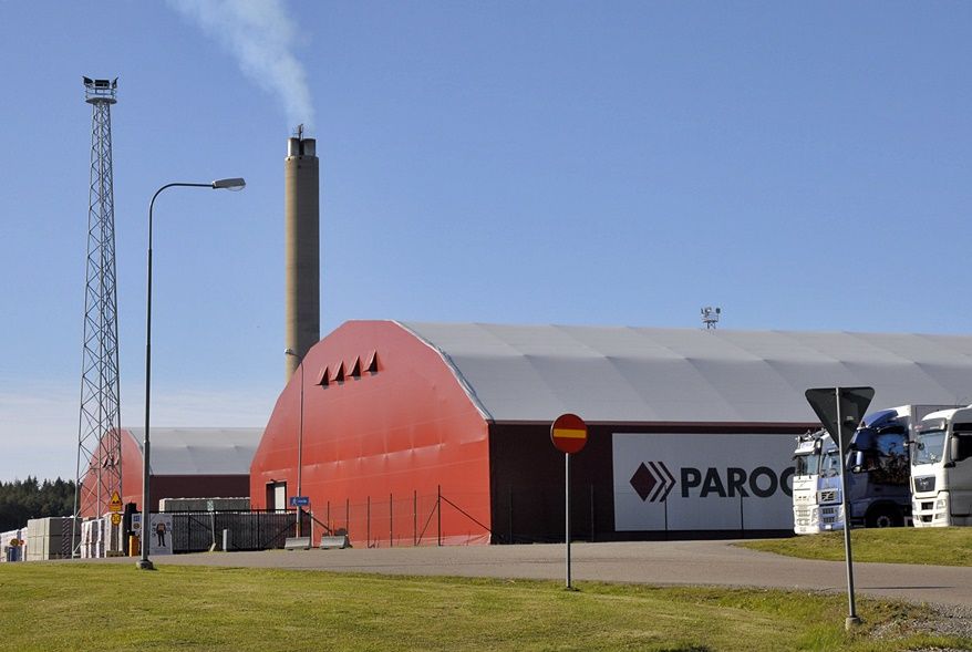 Industribyggnad med rött böjt tak, hög skorsten och PAROC-skylt under en klarblå himmel