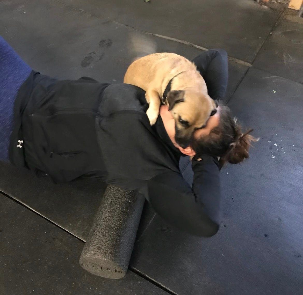 Person lying on a gym mat with a tan dog curled on their chest, indoors.