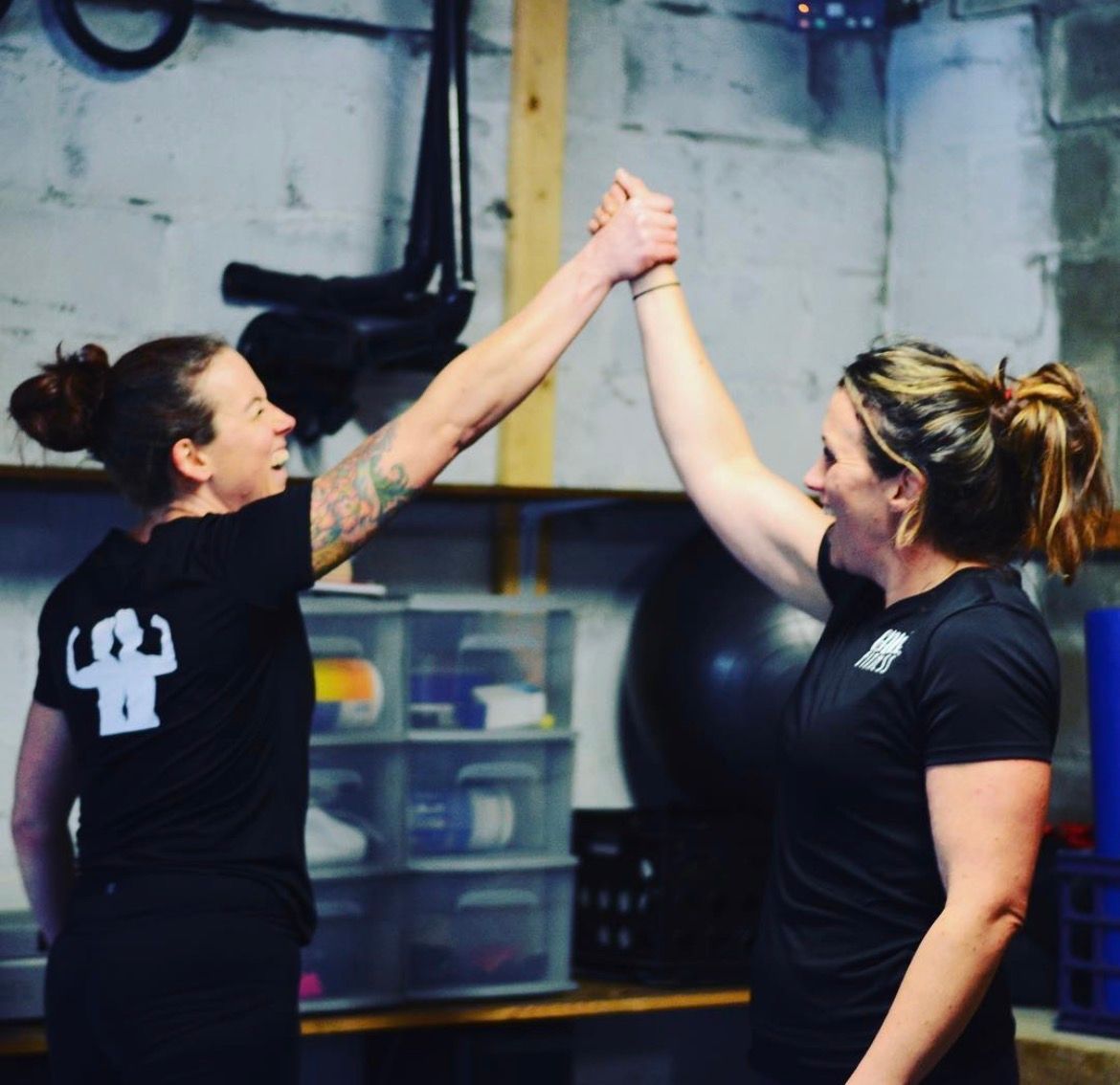 Two people in black shirts high-five in a gym, smiling and raising their arms.