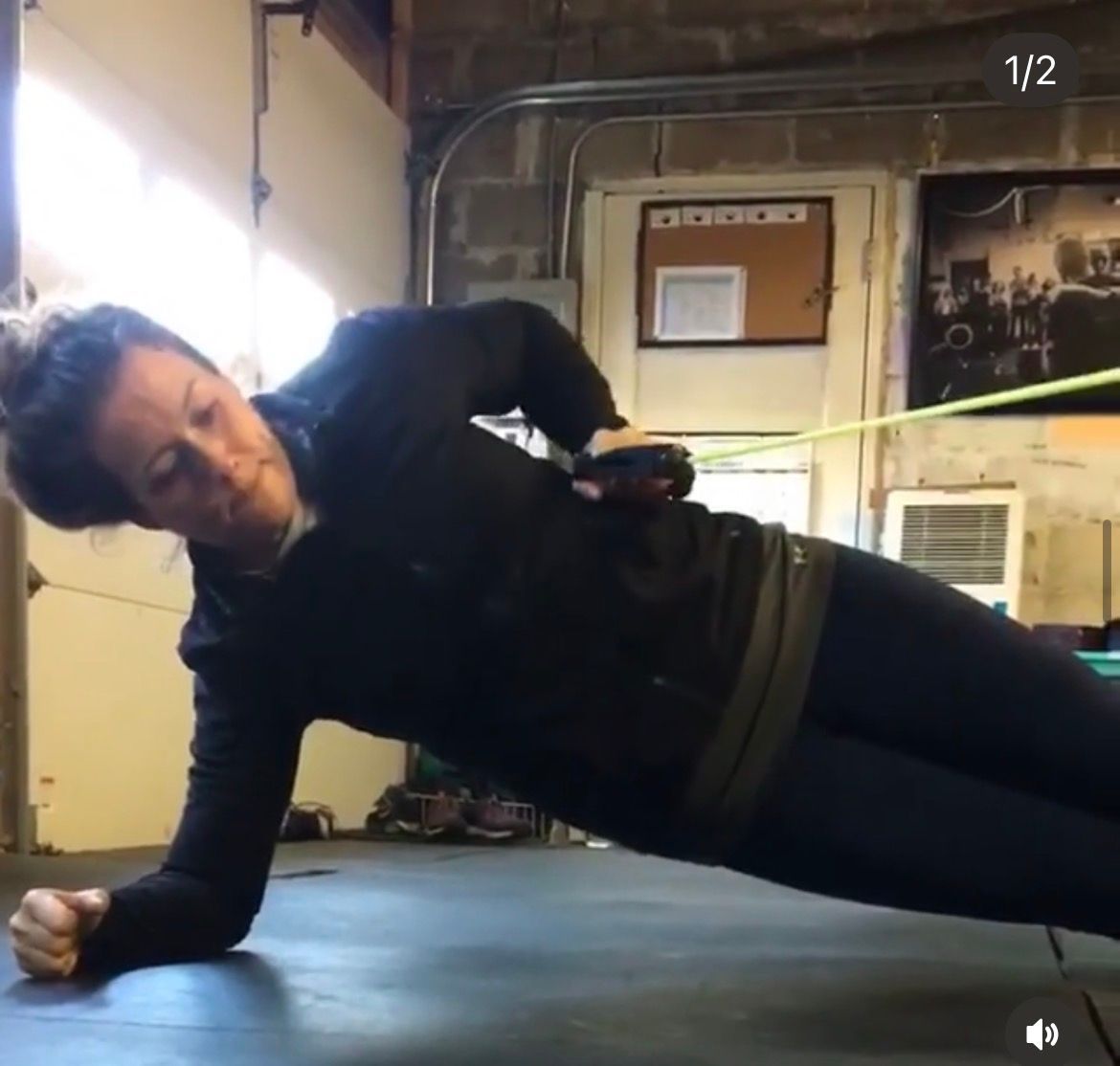 Person holding a side plank on a gym floor, wearing black workout clothes.