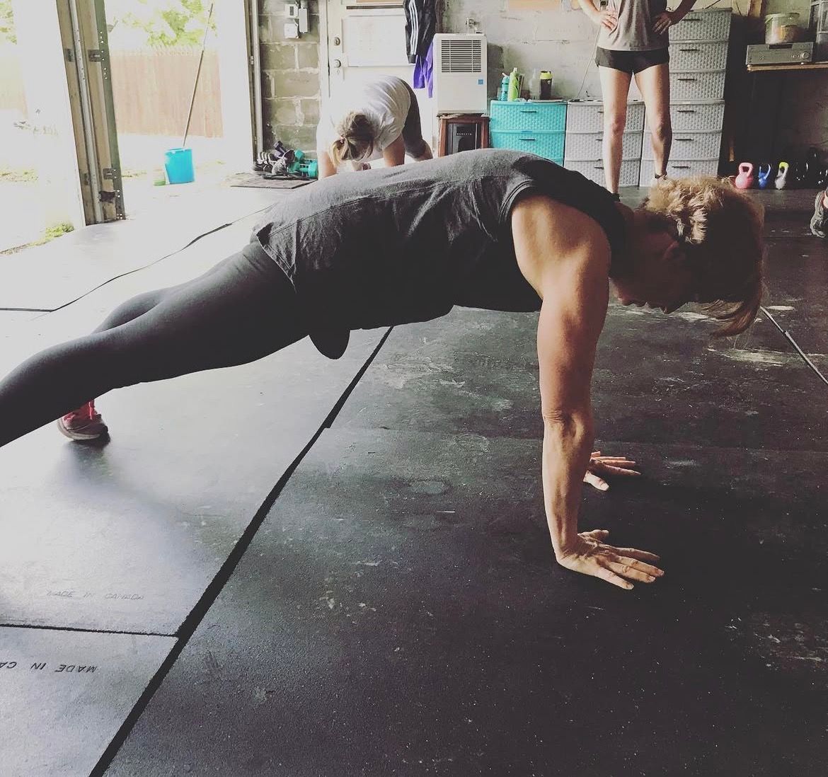 Person in a black workout outfit holding a plank on a gym floor.