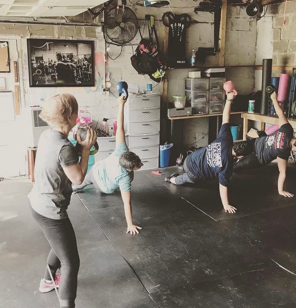 Group fitness class in a gym, with people balancing handstands and lifting weights.