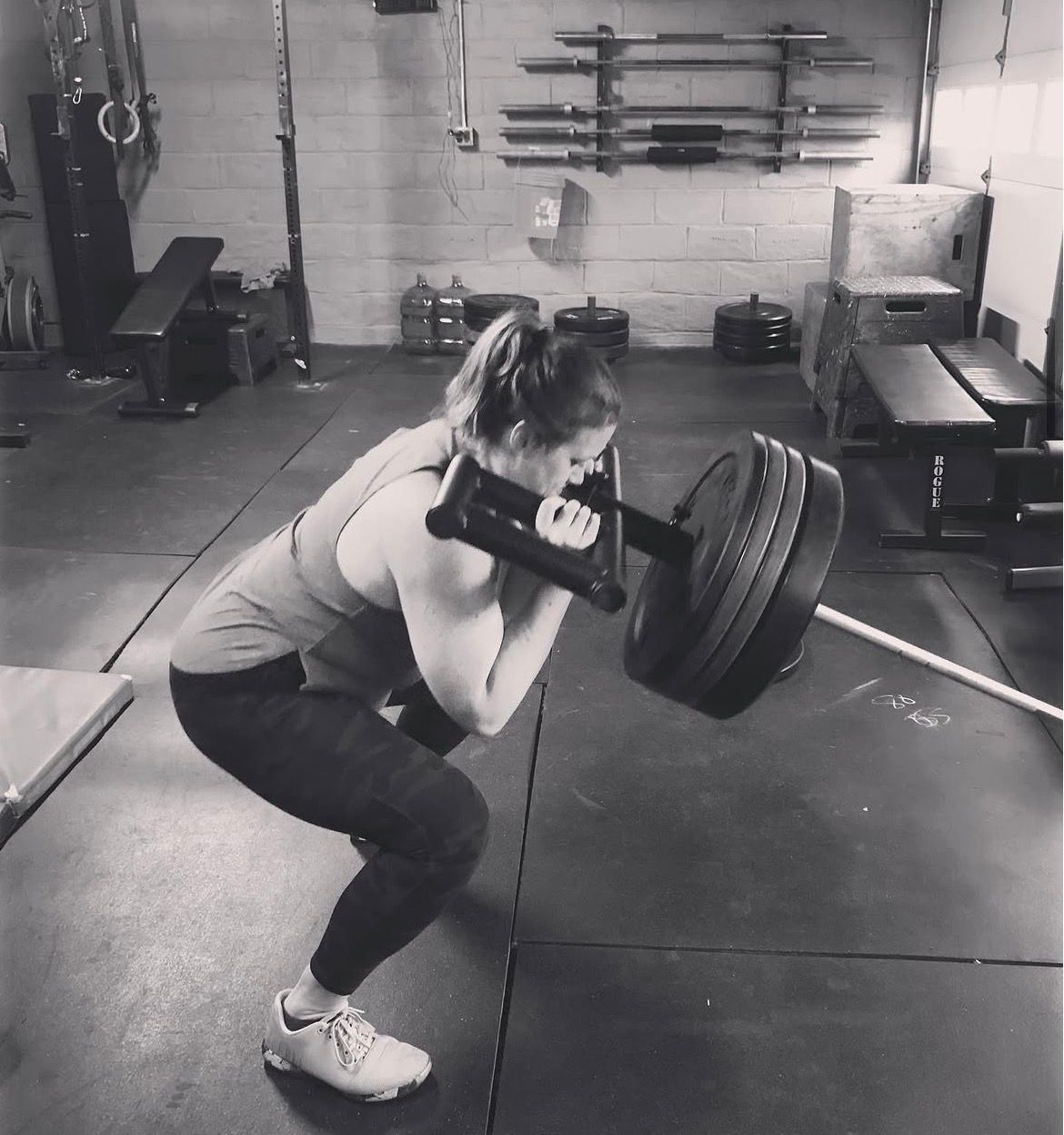 Woman doing a front squat with a dumbbell in a gym, wearing workout clothes.
