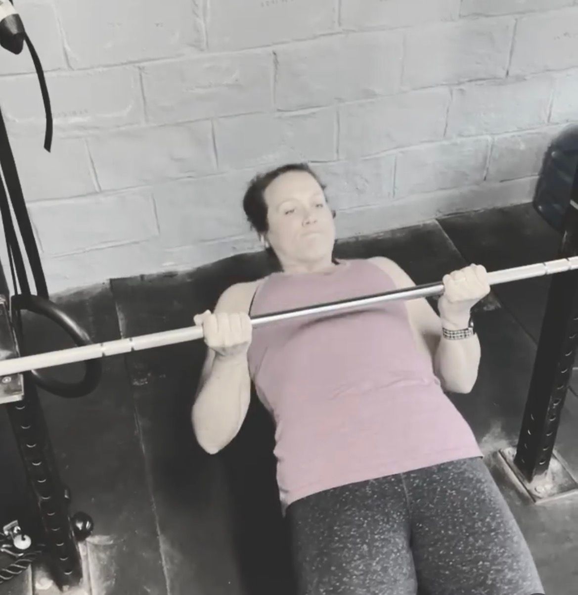 Person doing a bench press on an incline bench in a gym, wearing a pink shirt and gray leggings.