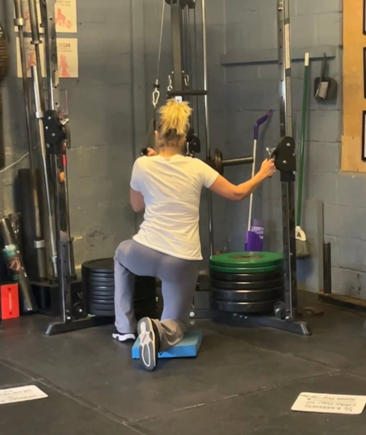 Person kneeling on a gym cable machine, exercising with arms extended in a workout area