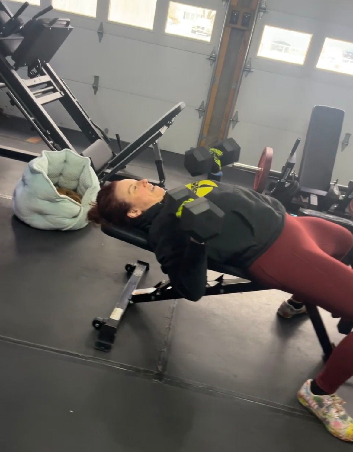 Person doing a bench bridge exercise in a gym, wearing black jacket and maroon leggings.