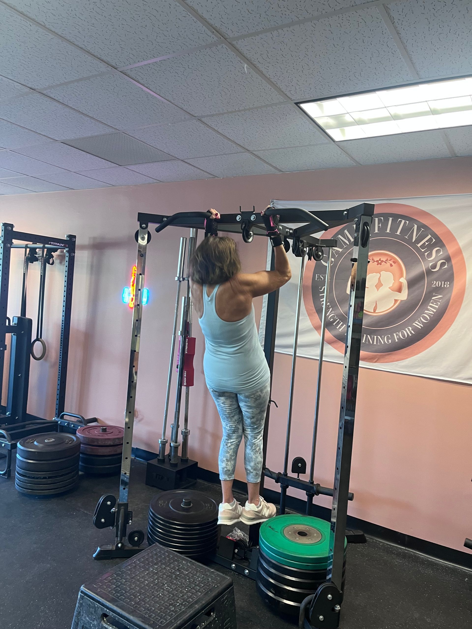 Person exercising on a pull-up rig in a gym, surrounded by plates and workout equipment.