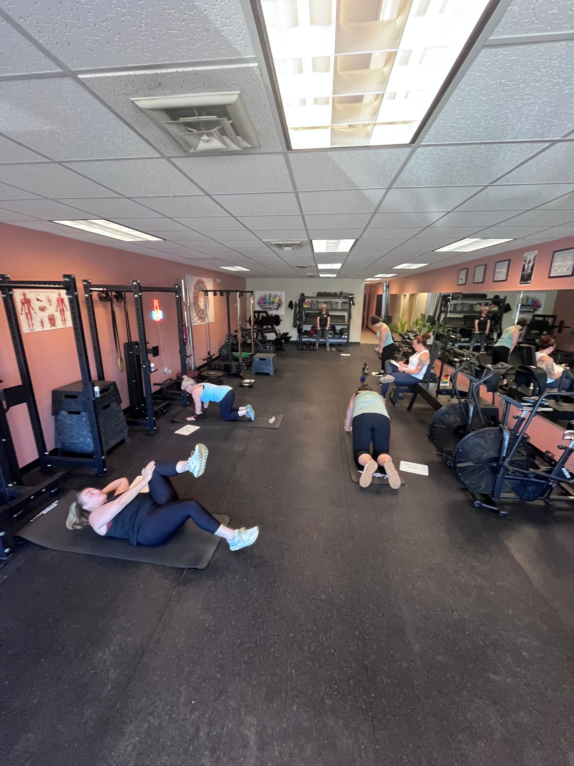 People exercising on mats in a gym, with equipment along the walls.