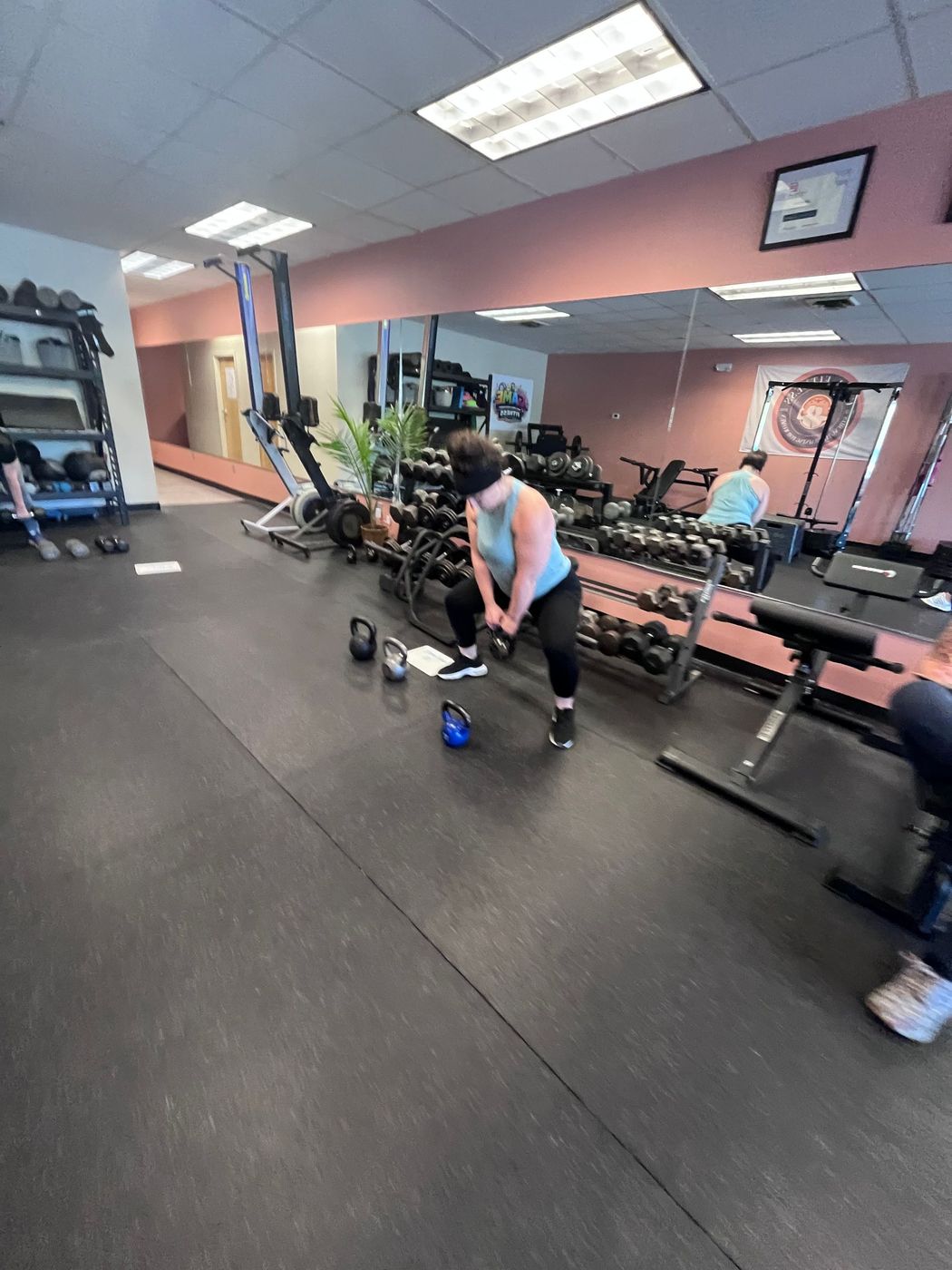 Person lifting dumbbells in a gym with mirrors, benches, and kettlebells.