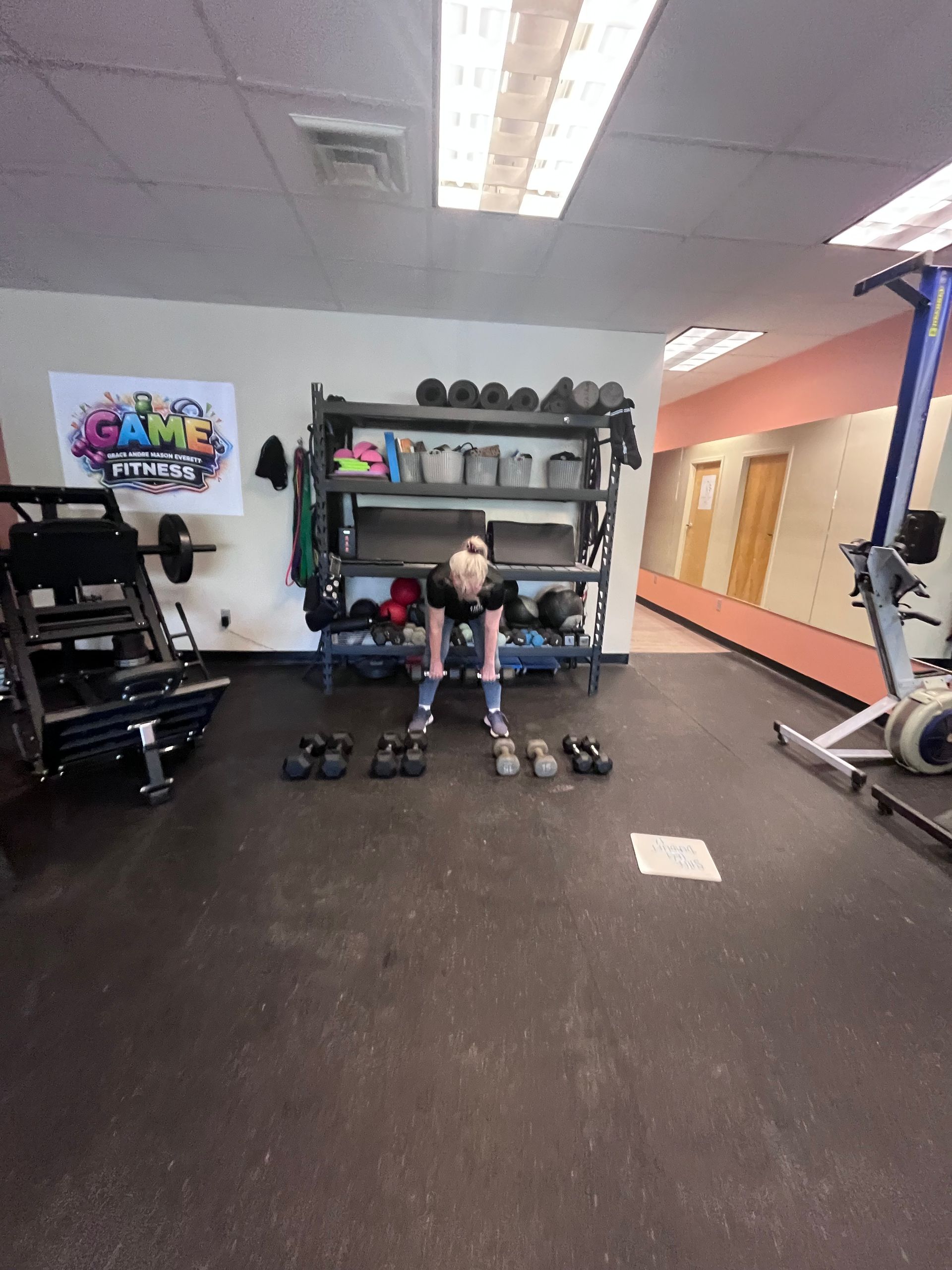 Person lifting dumbbells in a gym, with weights, racks, and exercise equipment in the background.
