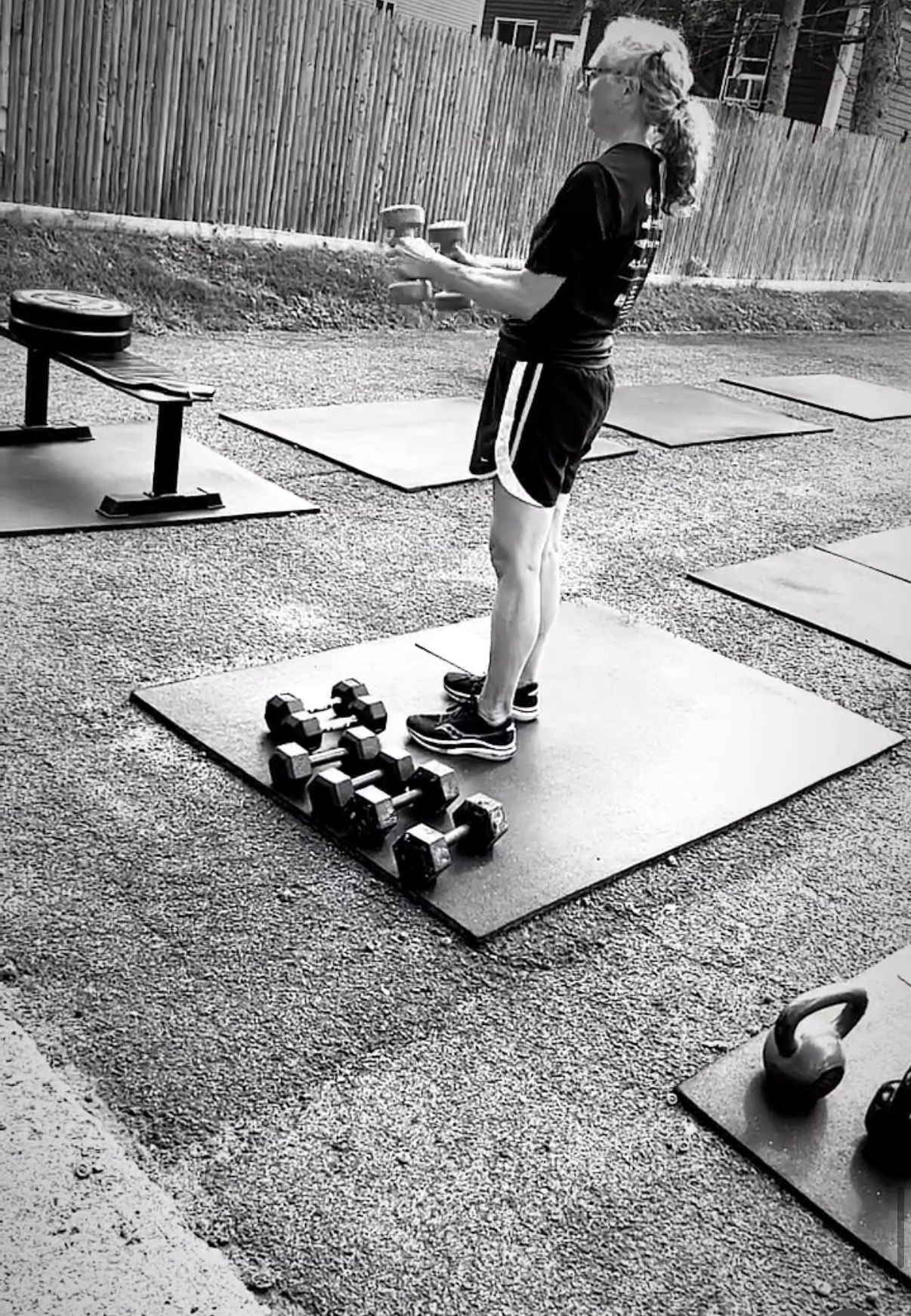 Person standing on exercise mat beside dumbbells in an outdoor workout area