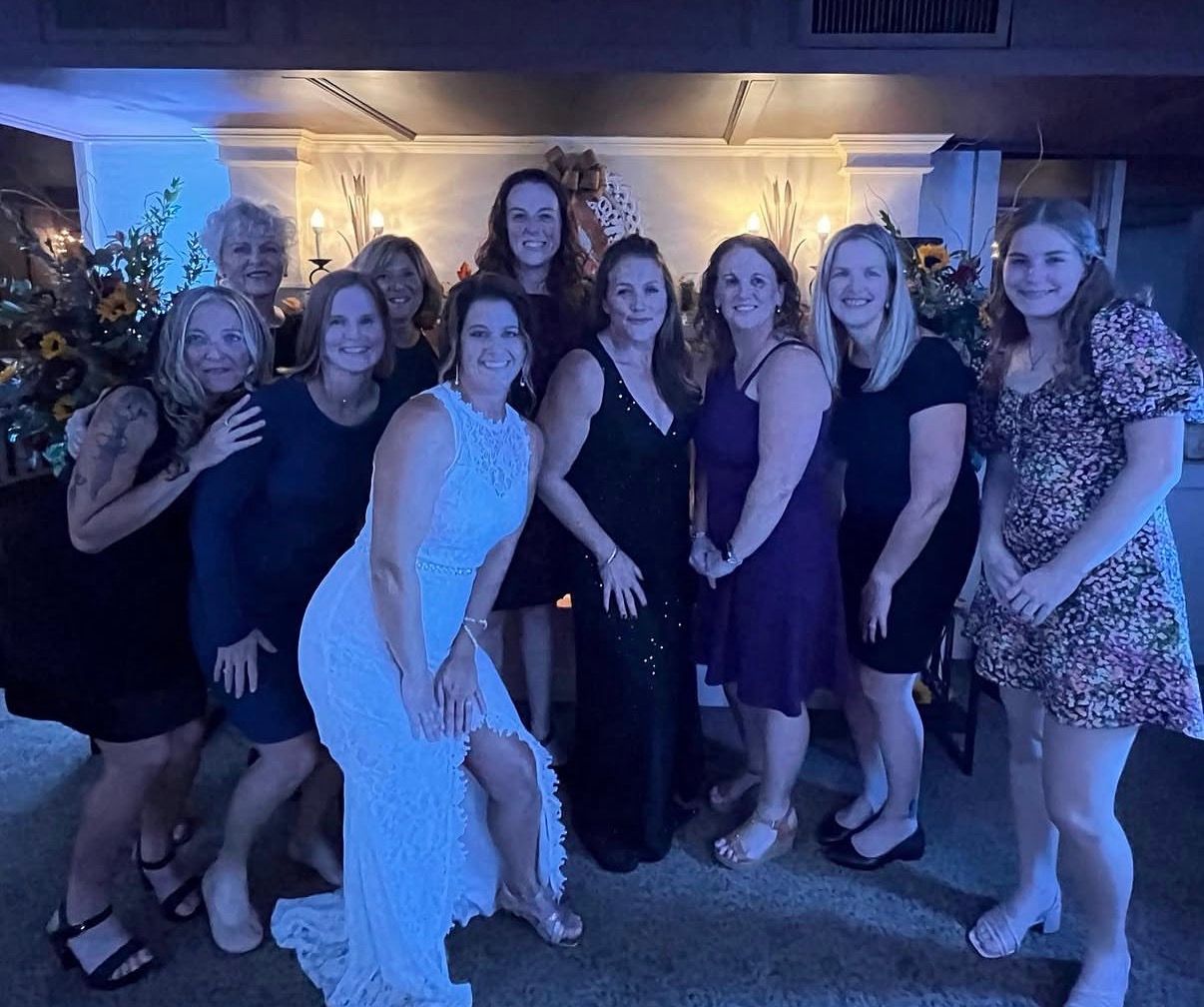 Group of people posing together at a dimly lit indoor party, with one woman in a white dress in front.