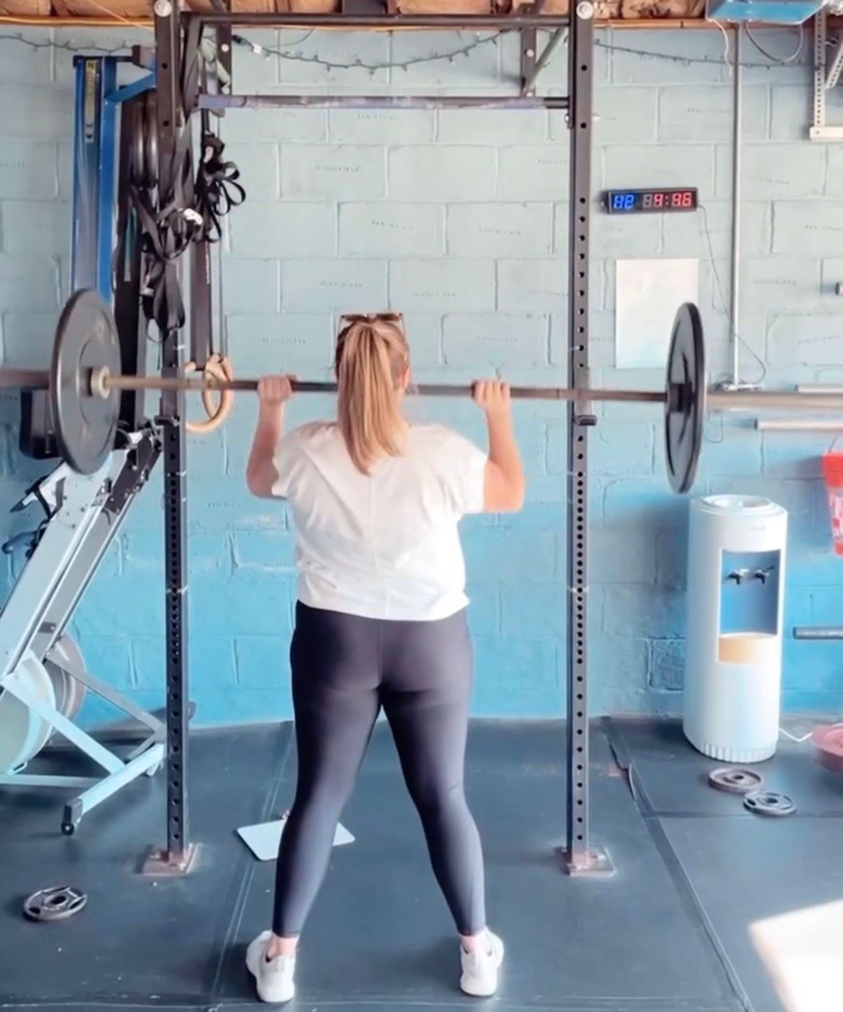 Person lifting a barbell in a gym, seen from behind, with weight plates on either side