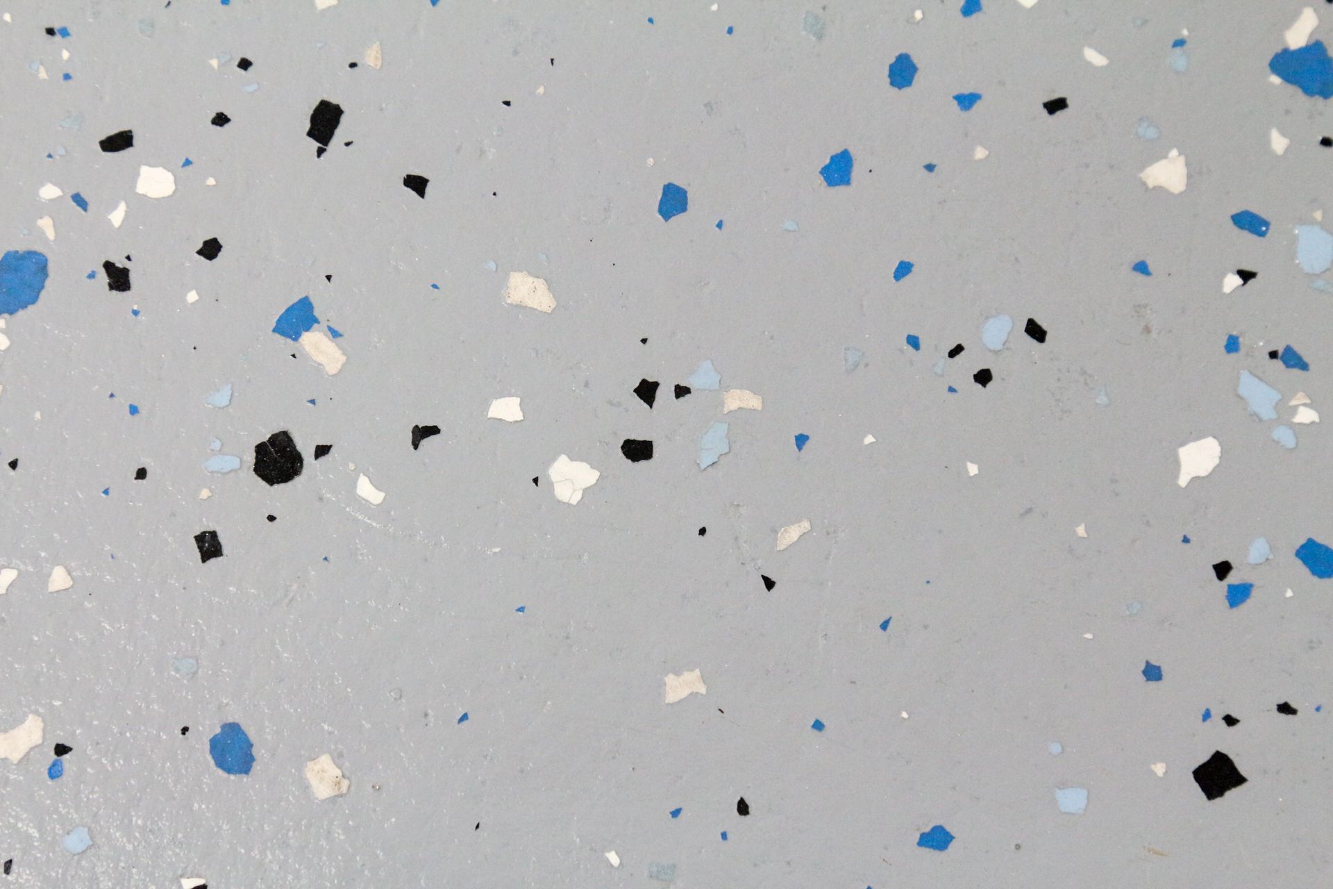 Light gray speckled surface with scattered black, white, and blue chips