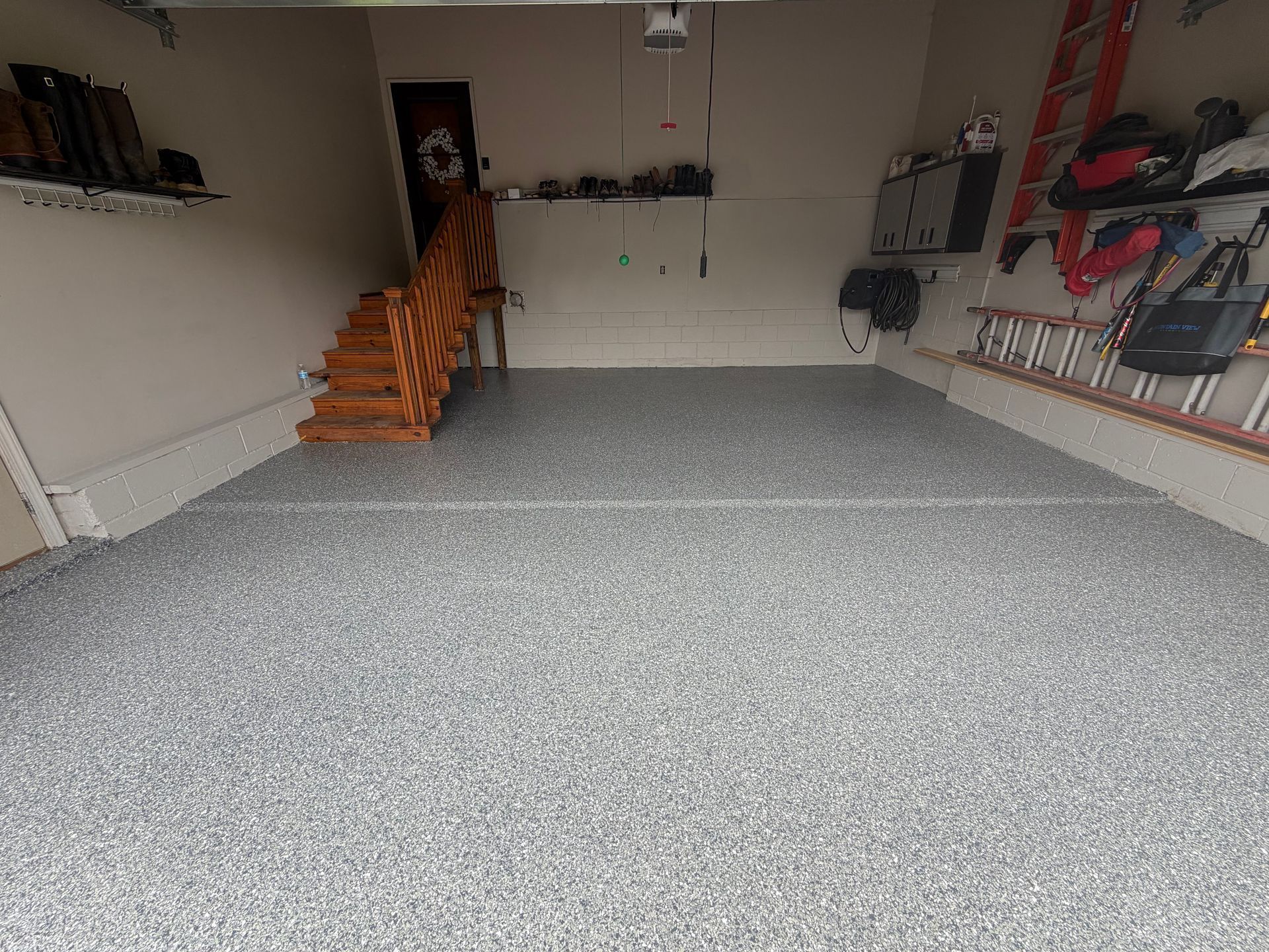 Empty garage with gray speckled floor and stairs leading to a side door.