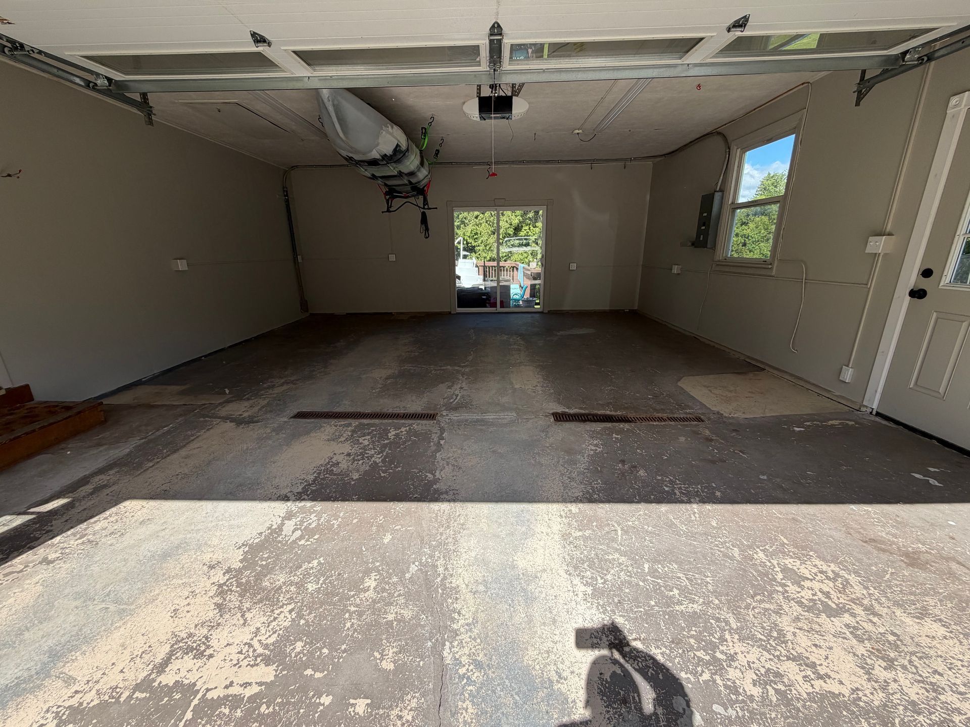 Interior of a damaged garage with torn ceiling, exposed insulation, and debris-stained concrete floor.