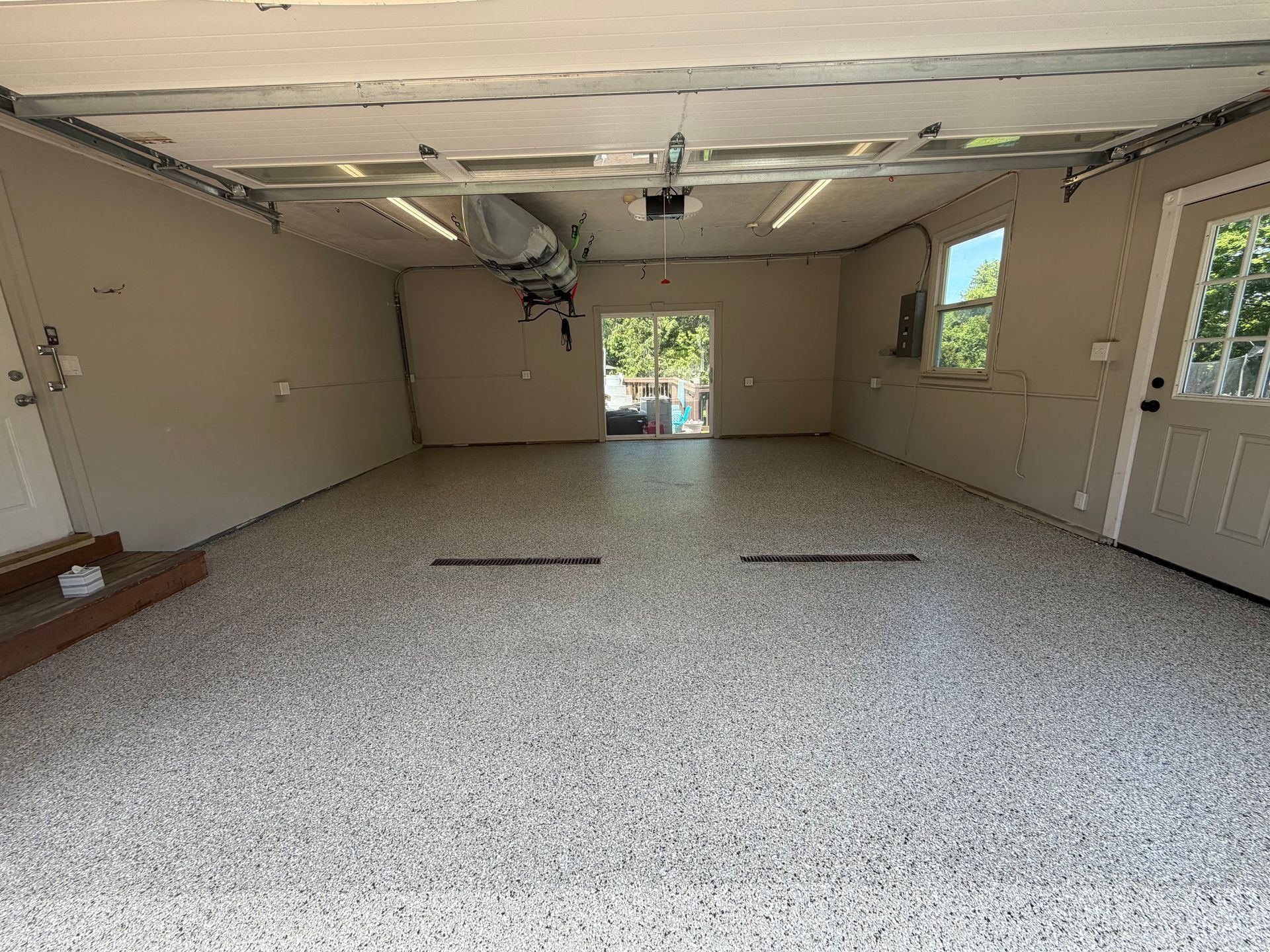 Empty garage with speckled floor, beige walls, and ceiling damage near open double doors.