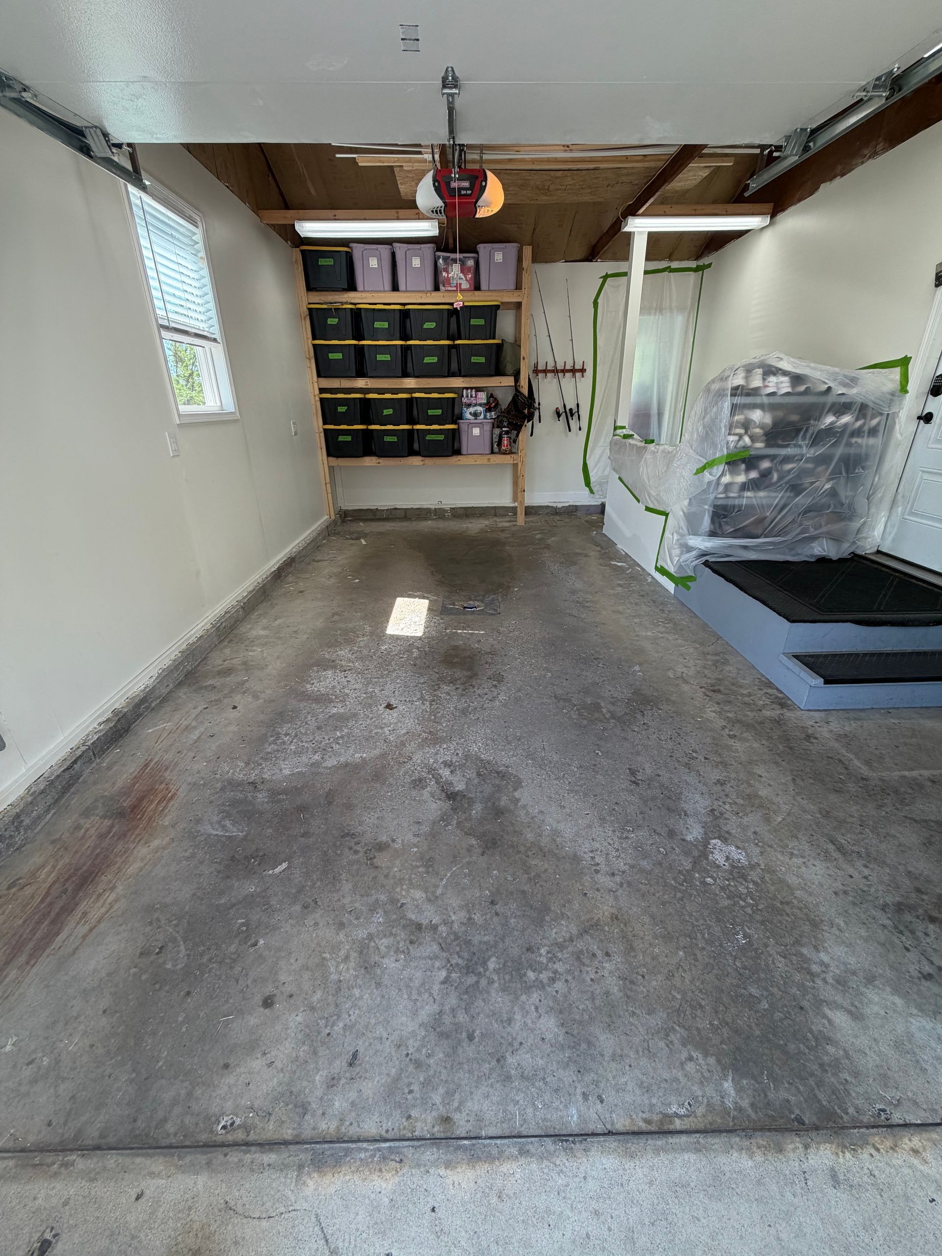 Empty garage with concrete floor, shelves at back, and stacked storage bins on the right.