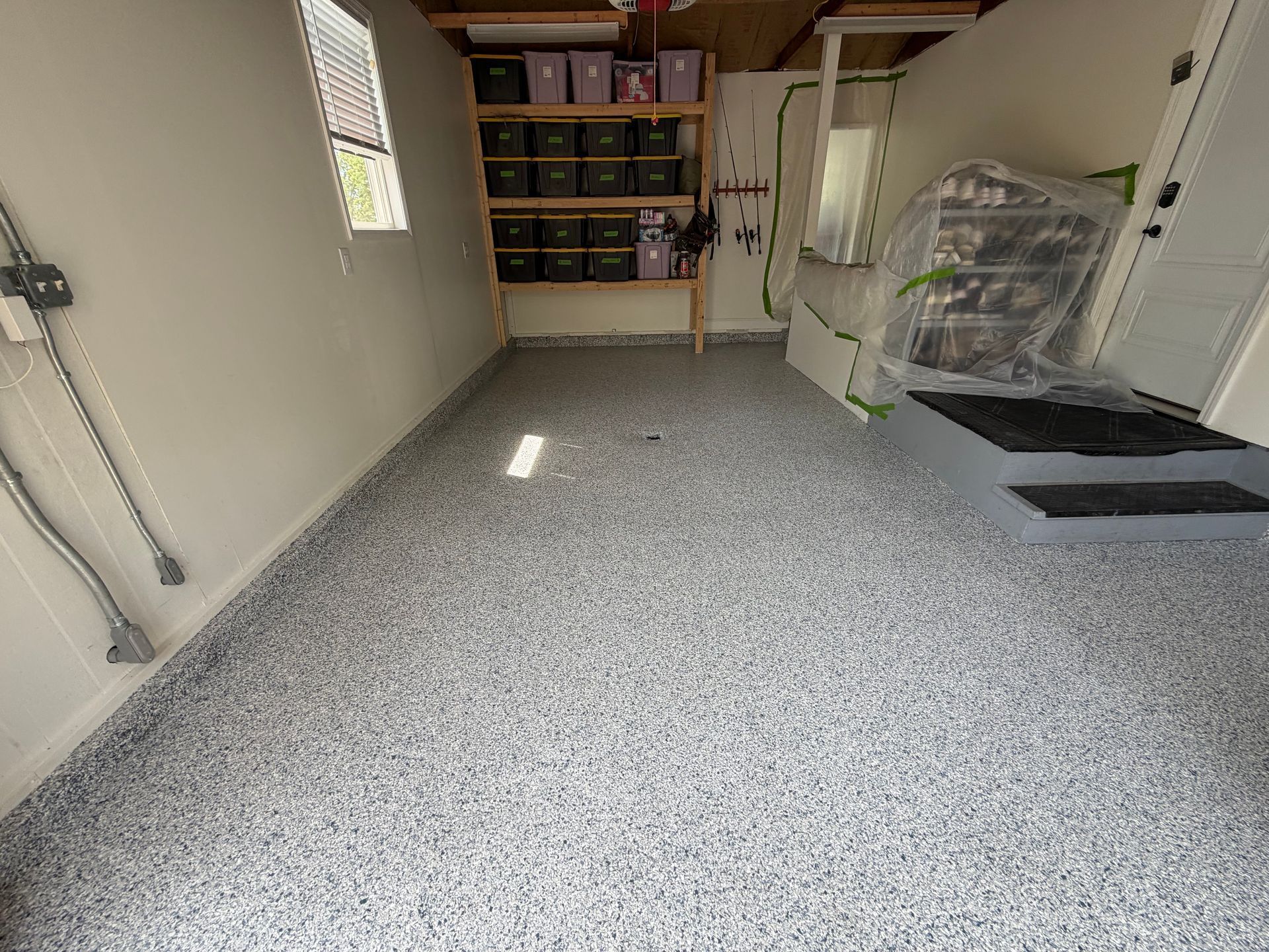 Garage with speckled epoxy floor, storage shelves, freezer, and bike under a cover.