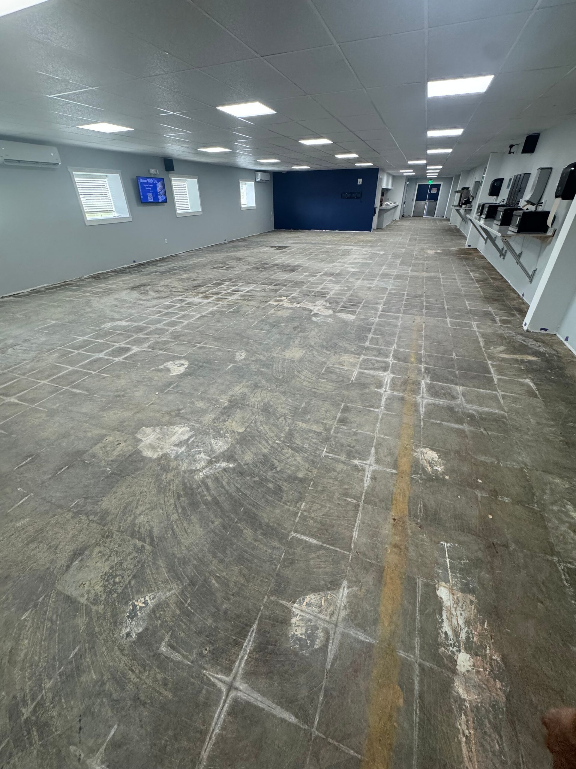 Empty indoor room with a worn concrete floor and white walls, lit by ceiling lights.