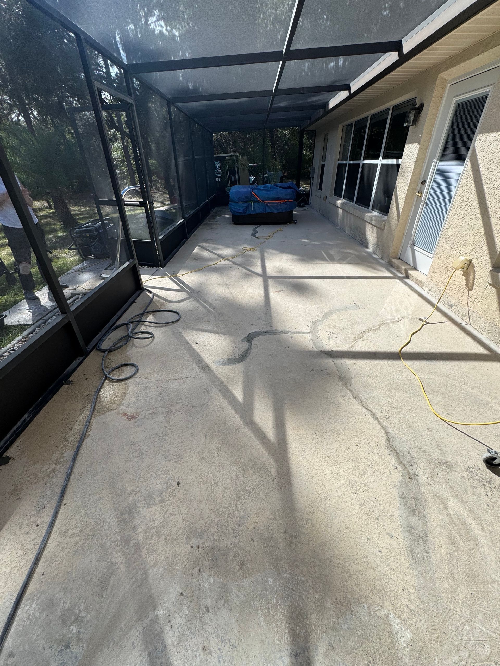 Covered patio walkway beside a brick building, with a blue cart at the far end and shadowed netting on the left.