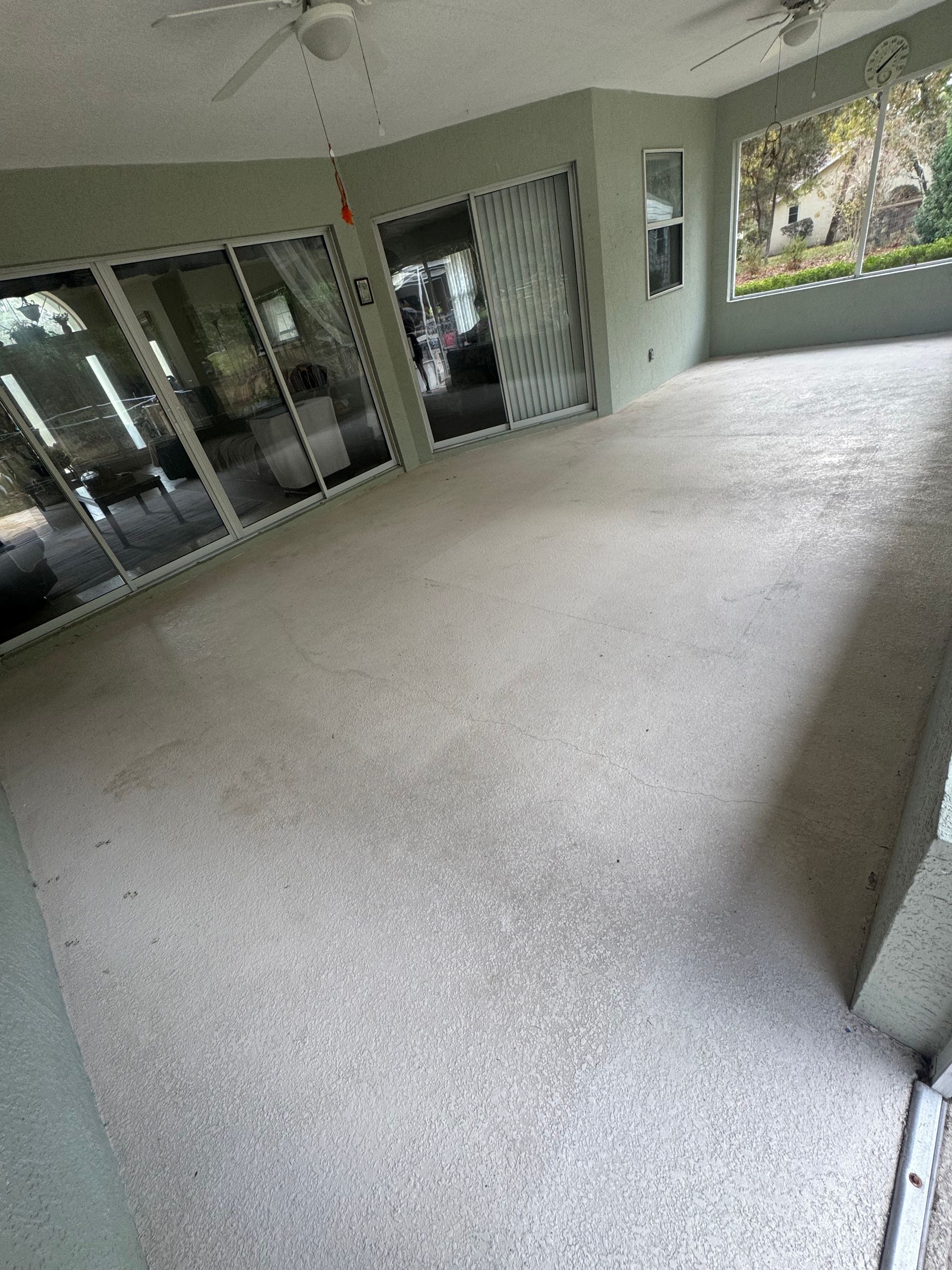 Covered patio with white textured floor, glass sliding doors, and a view of greenery outside