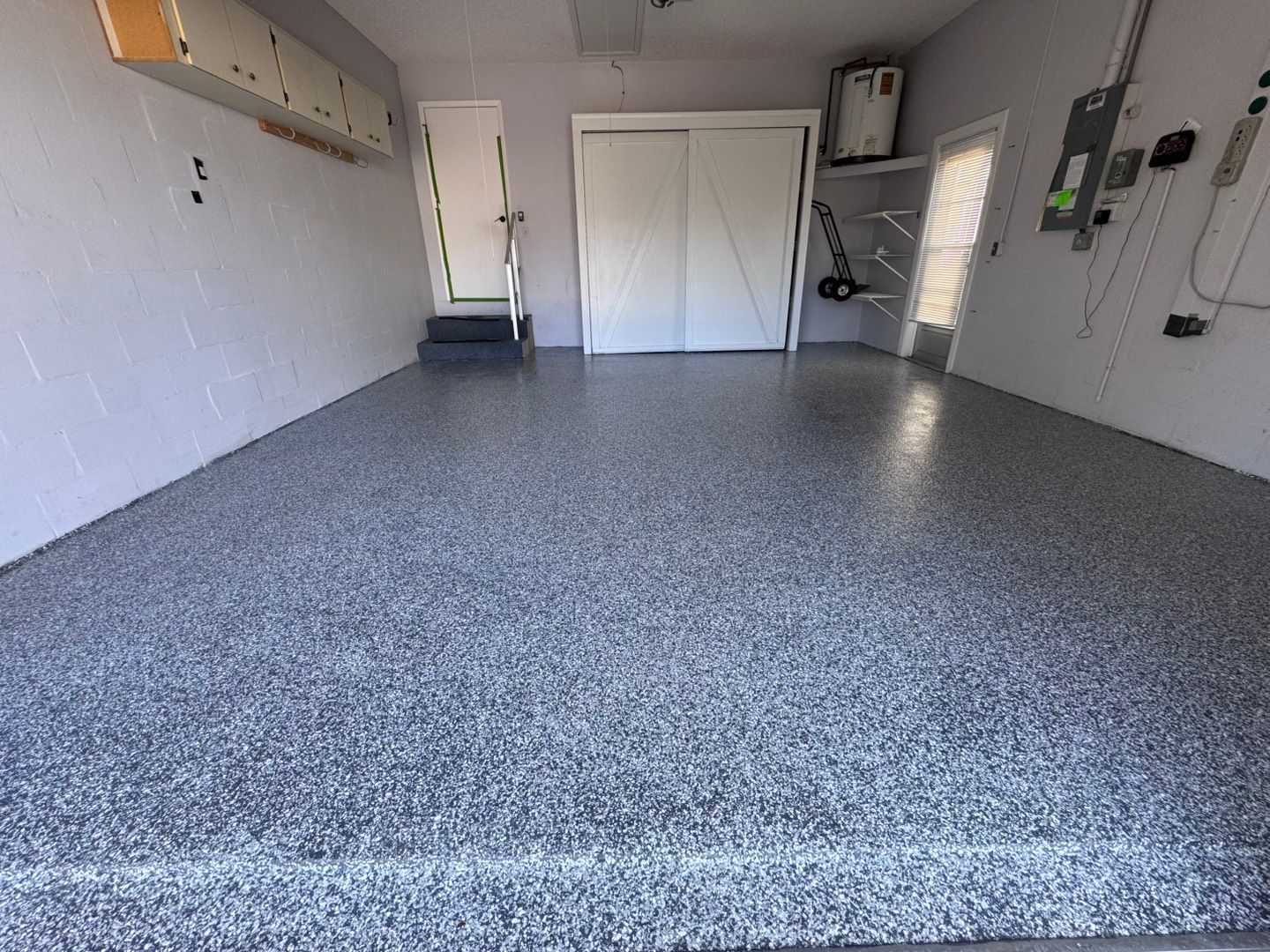 Empty garage with speckled epoxy floor and white storage doors inside.